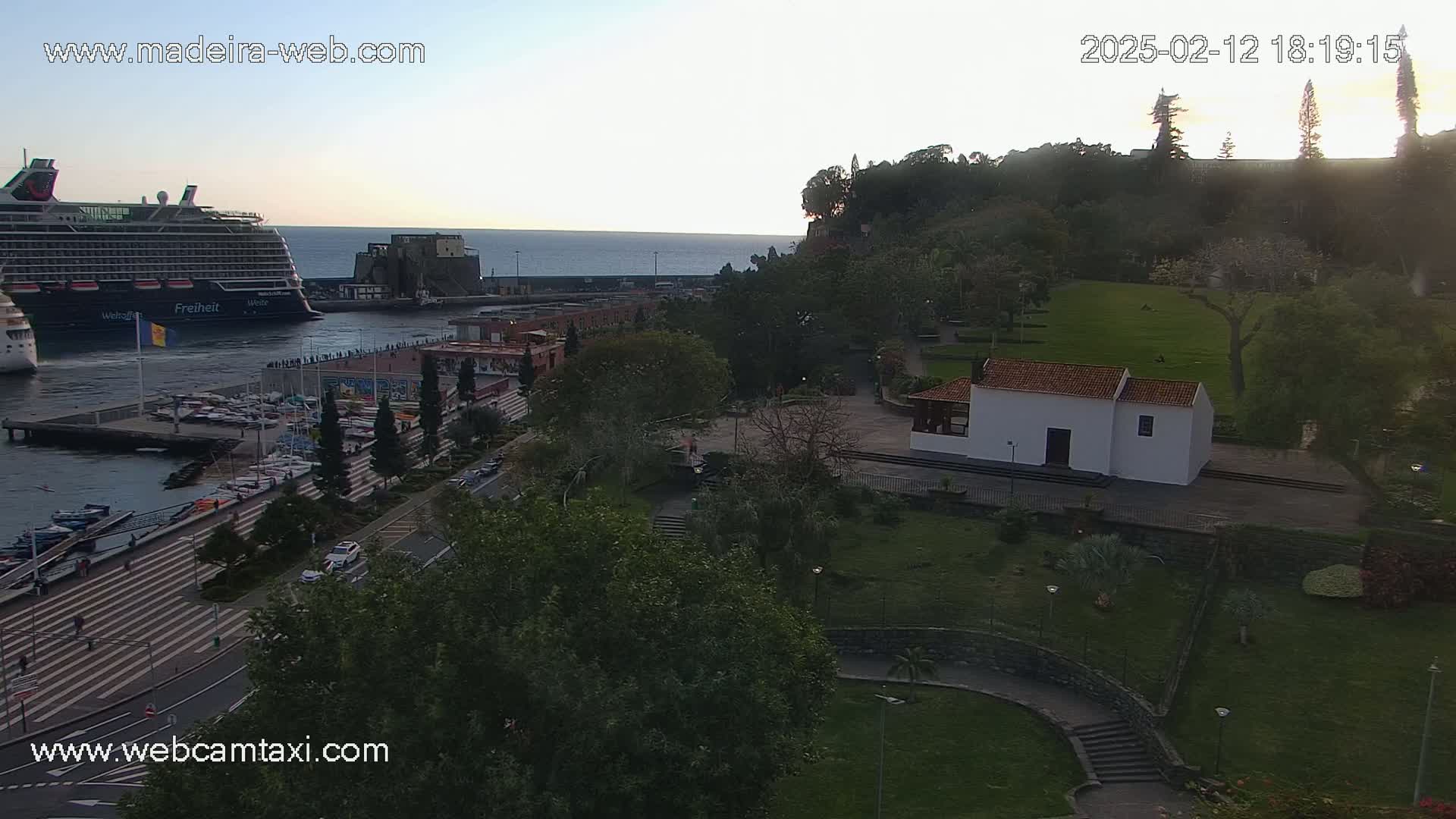 A cruise ship is docked at a harbor next to a park with a small white building, all under a twilight sky.
