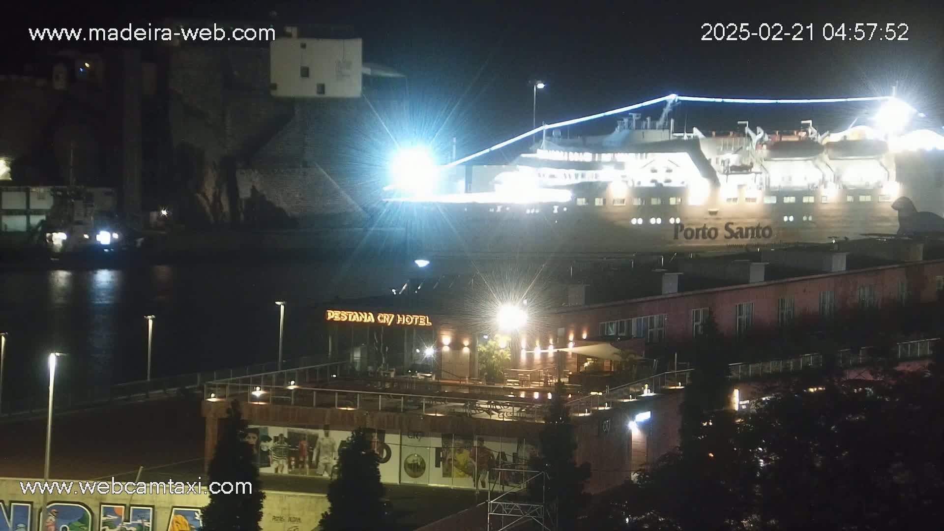 A brightly lit ferry named Porto Santo is docked at night near a building with outdoor seating.