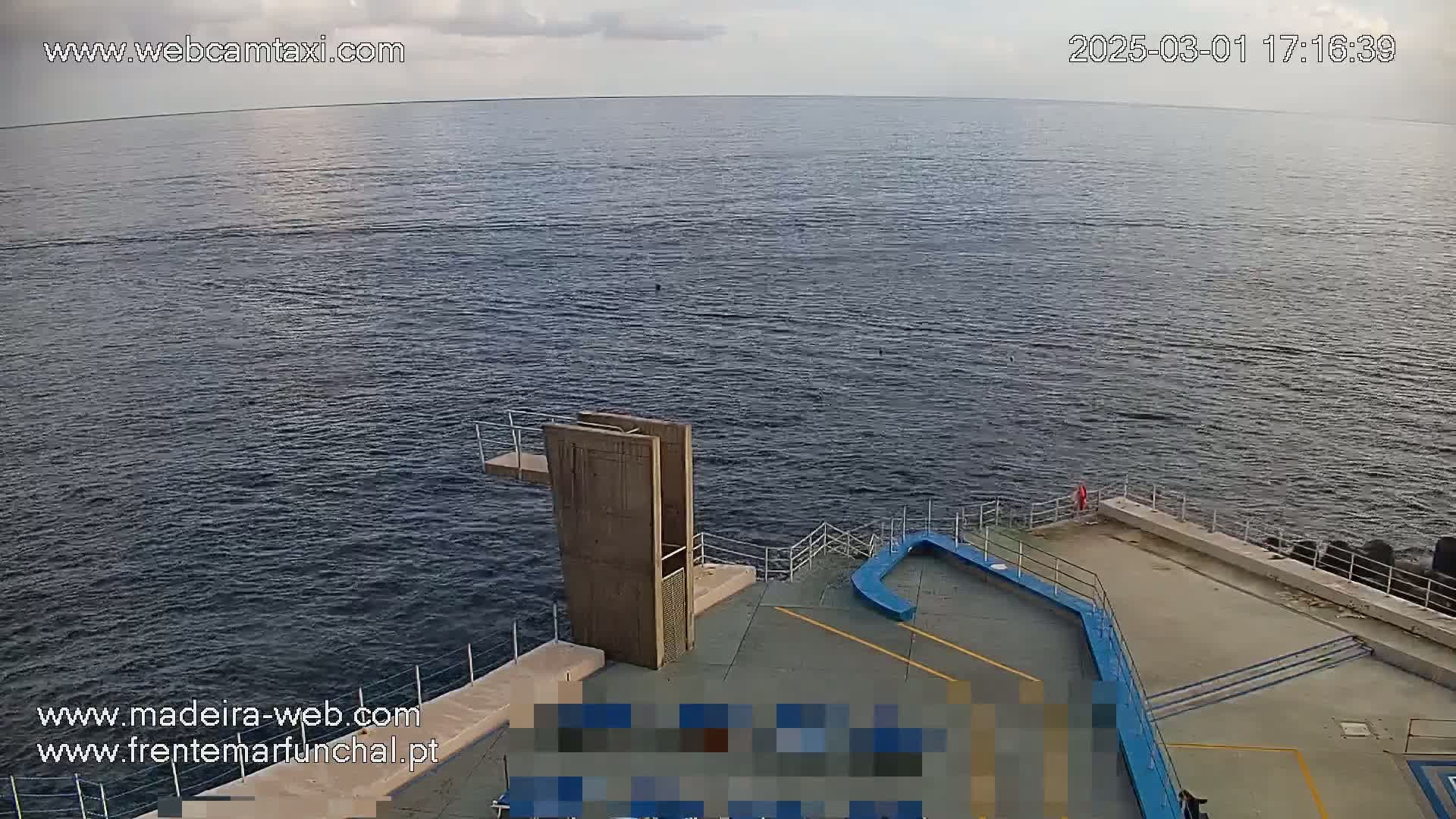 A diving platform overlooks a calm, dark-blue ocean under a partly cloudy sky.