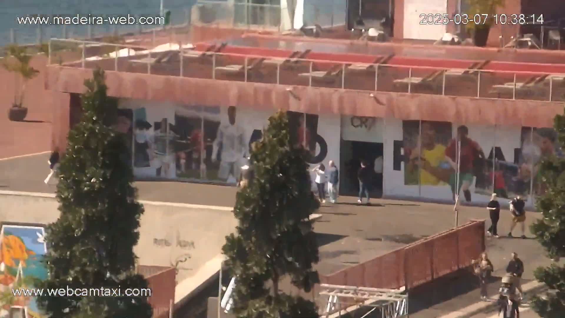 A sunny day reveals a building with large murals of athletes, several people walking around the area, and trees beside it.