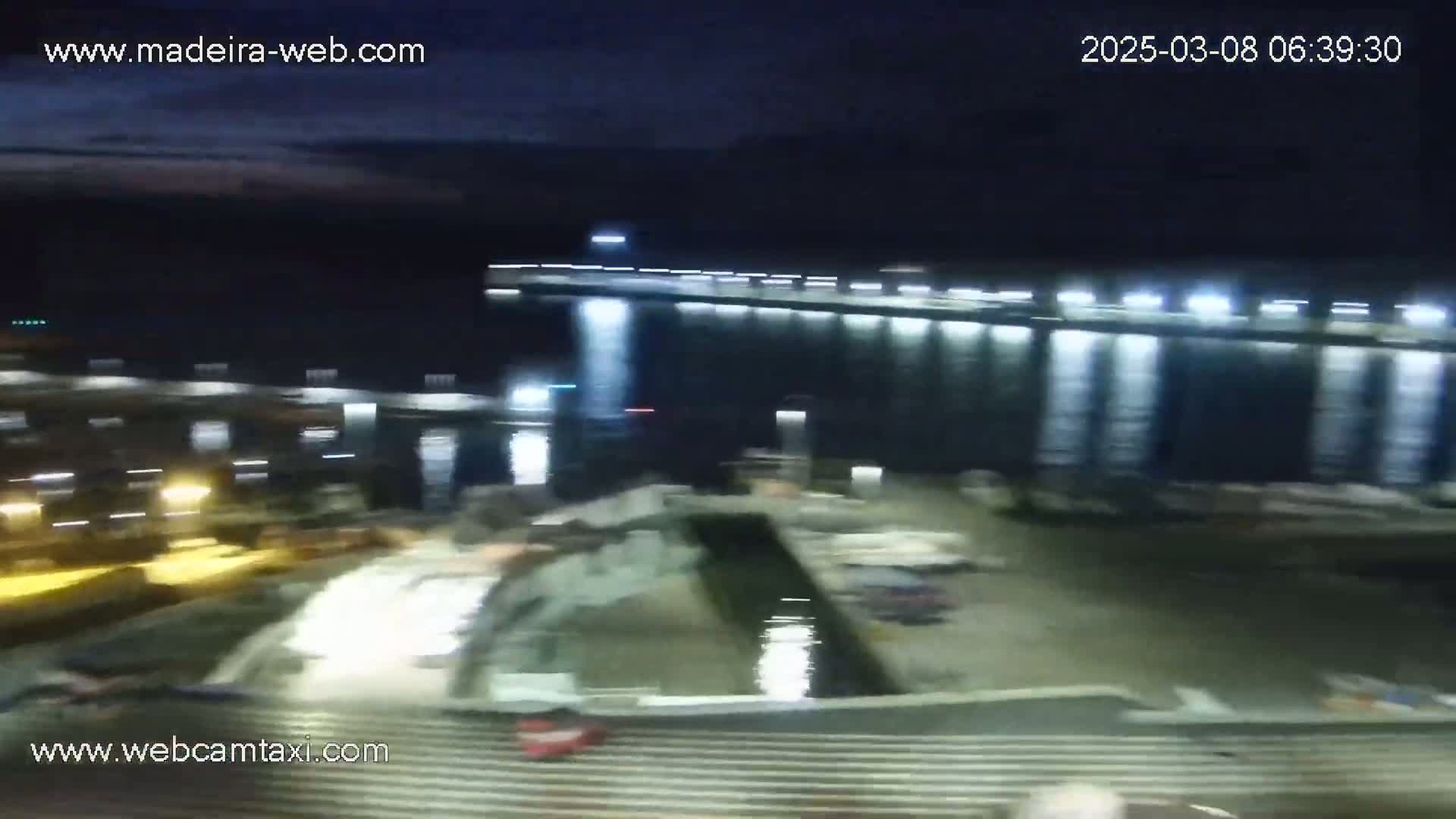 A nighttime, blurry view of a harbor with a large, illuminated structure and a body of dark water.