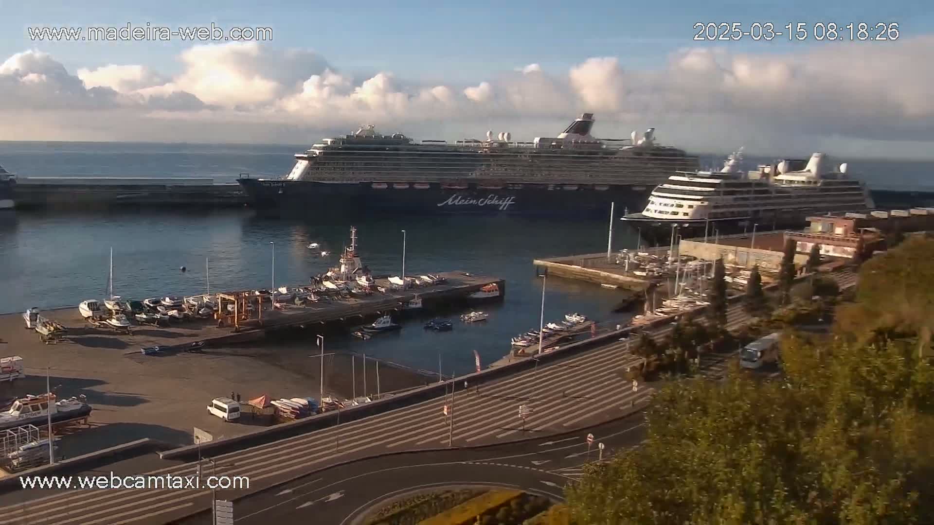 A harbor with several cruise ships and smaller boats docked, under a partly cloudy sky.