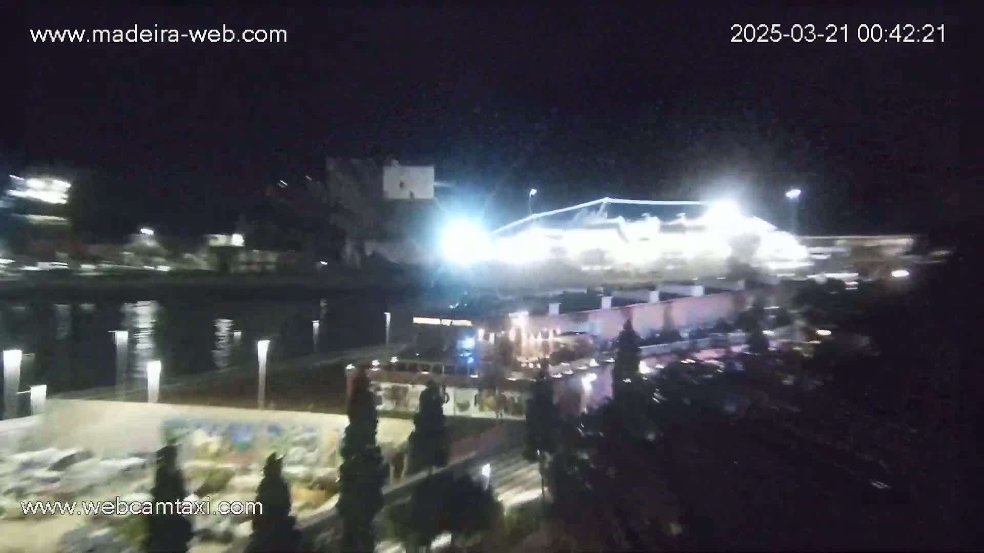 A nighttime view of a waterfront area with brightly lit buildings and a body of calm water reflecting the lights.