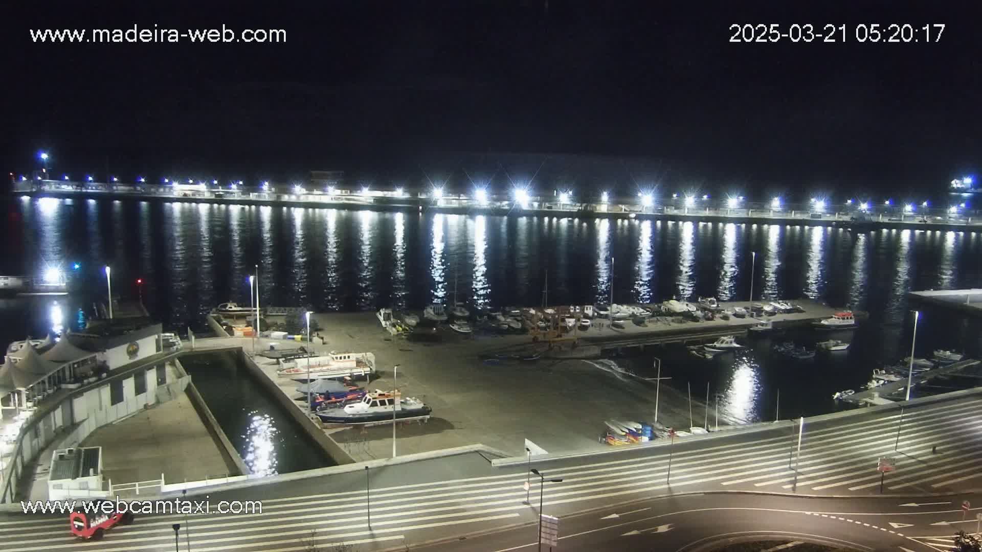 A brightly lit marina at night, filled with boats and calm water reflecting the lights.