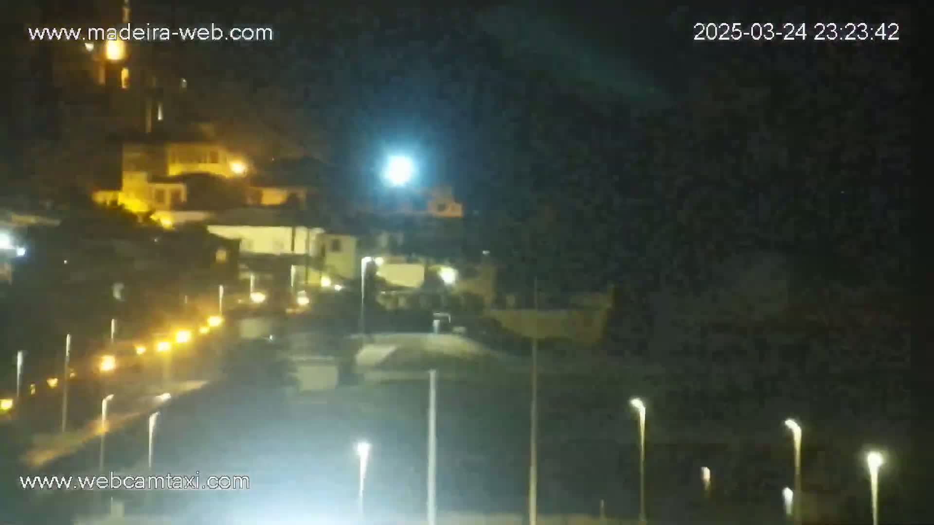 A nighttime long shot shows a hilly area with buildings and streetlights, illuminated under a mostly clear sky.
