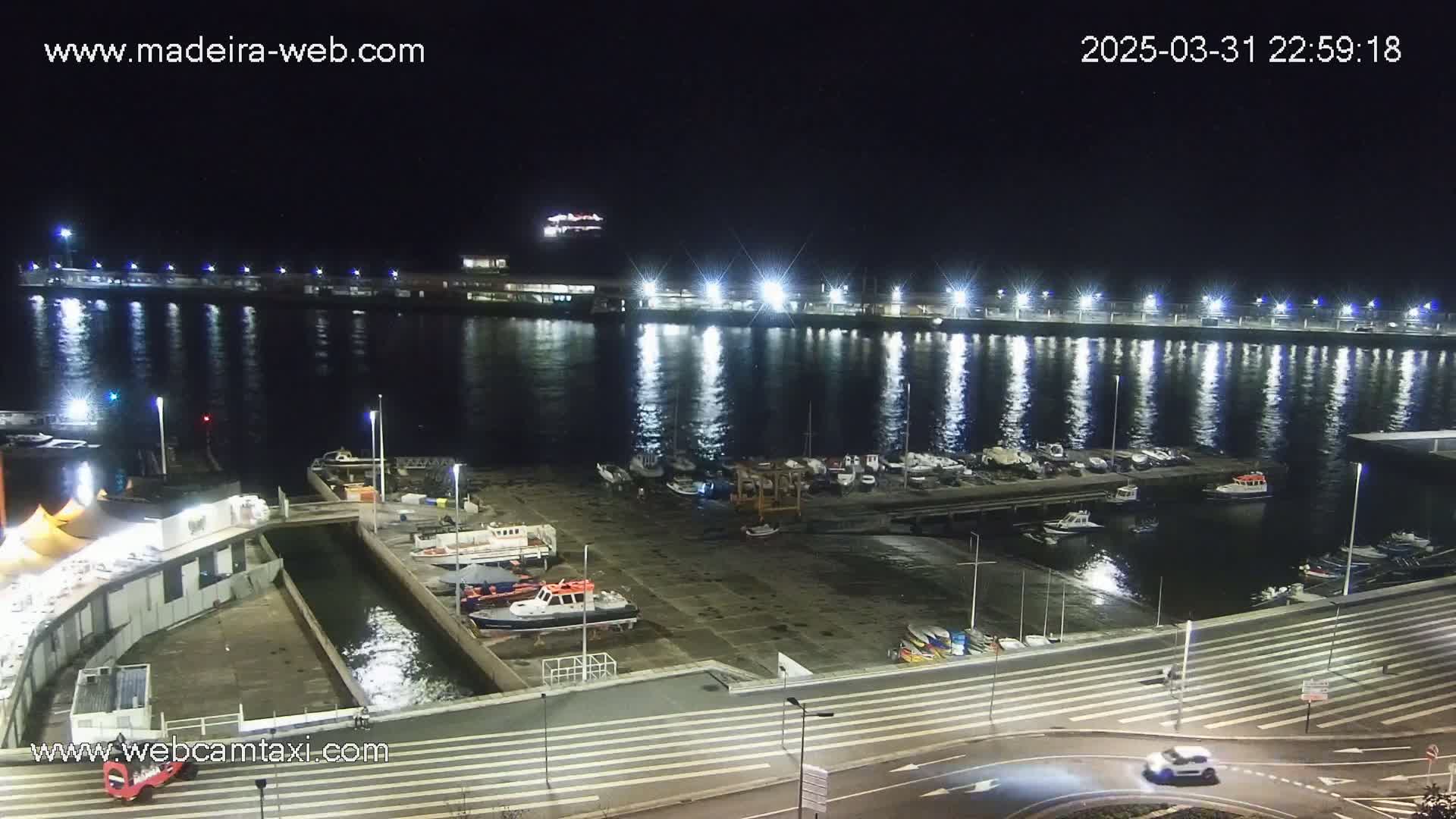 A brightly lit harbor at night, filled with docked boats and calm water reflecting the lights.