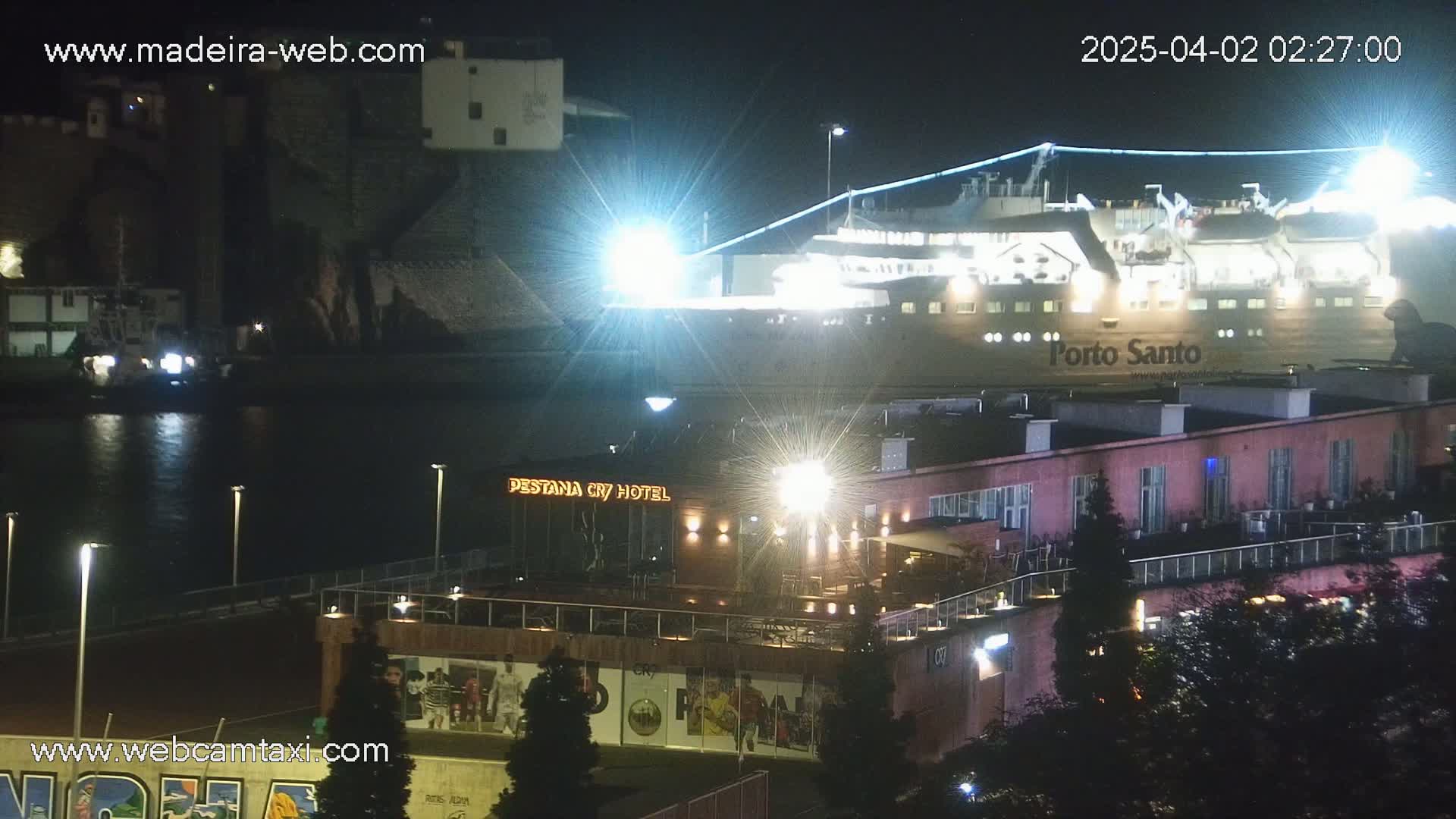 A brightly lit ferry named Porto Santo is docked at night next to a hotel and other buildings.