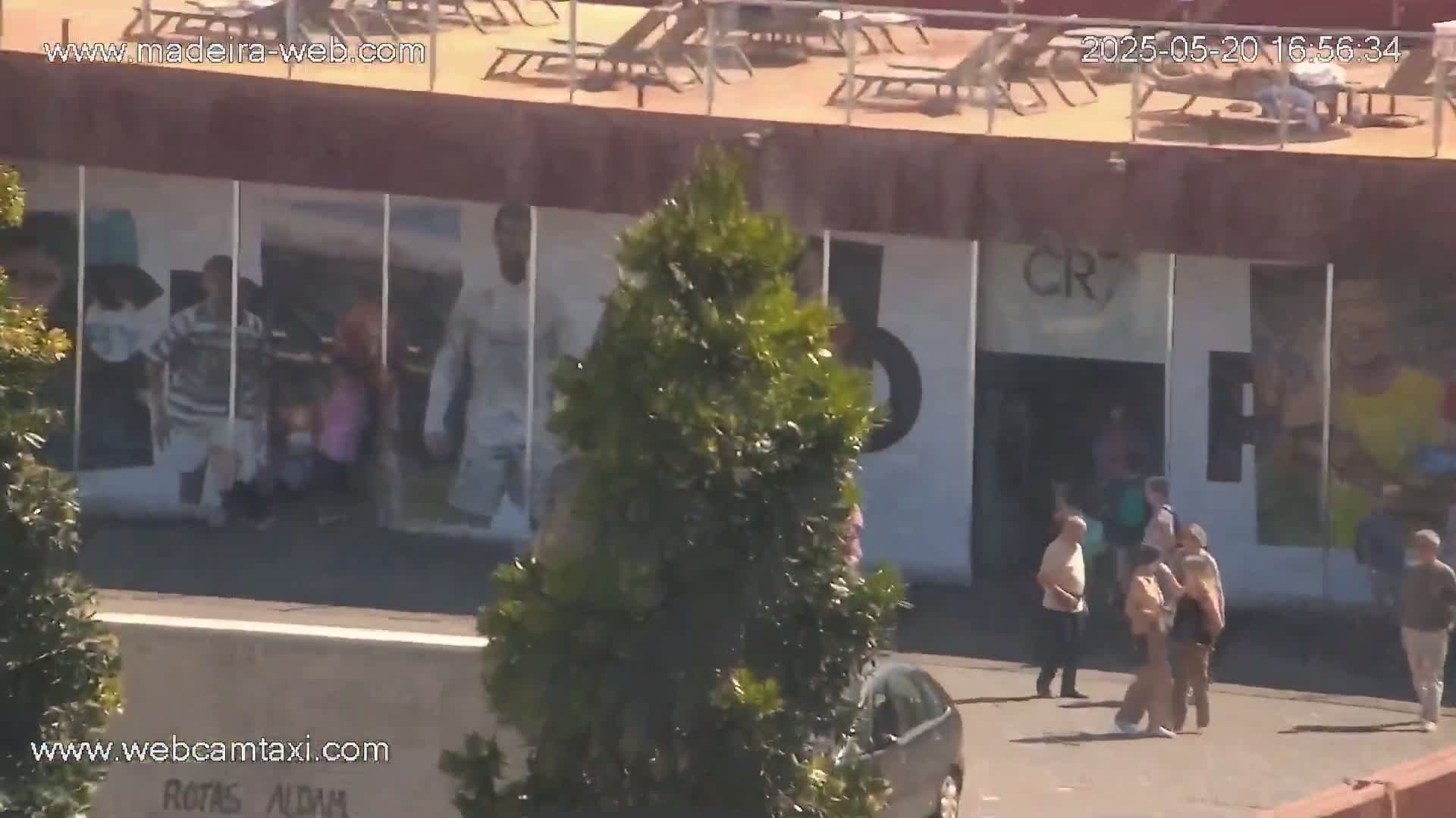 A building with a rooftop patio and large murals, featuring several people standing outside on a sunny day.