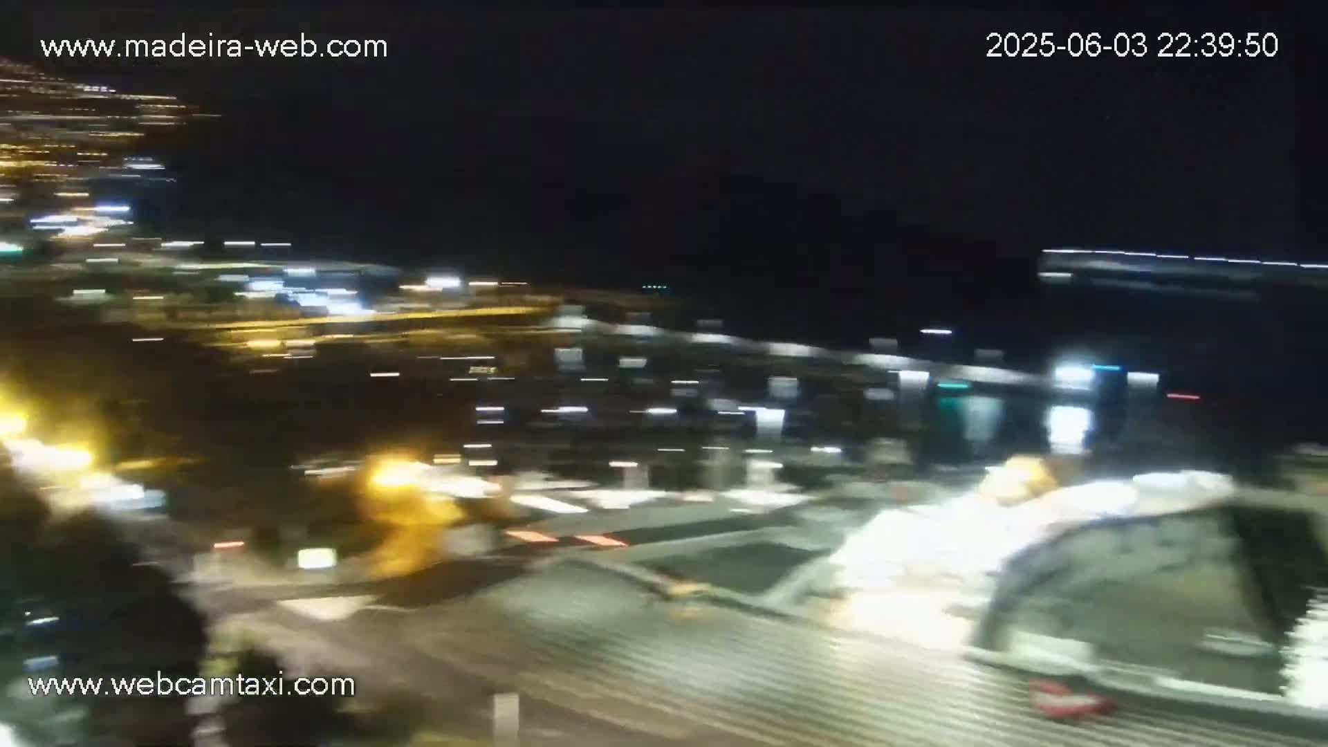 A nighttime, blurry view of a city harbor with lights from buildings and vehicles, appearing slightly out of focus.