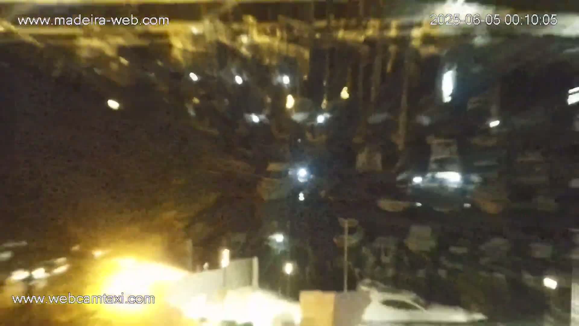 A nighttime, blurry view of a parking lot with cars and some lights visible.