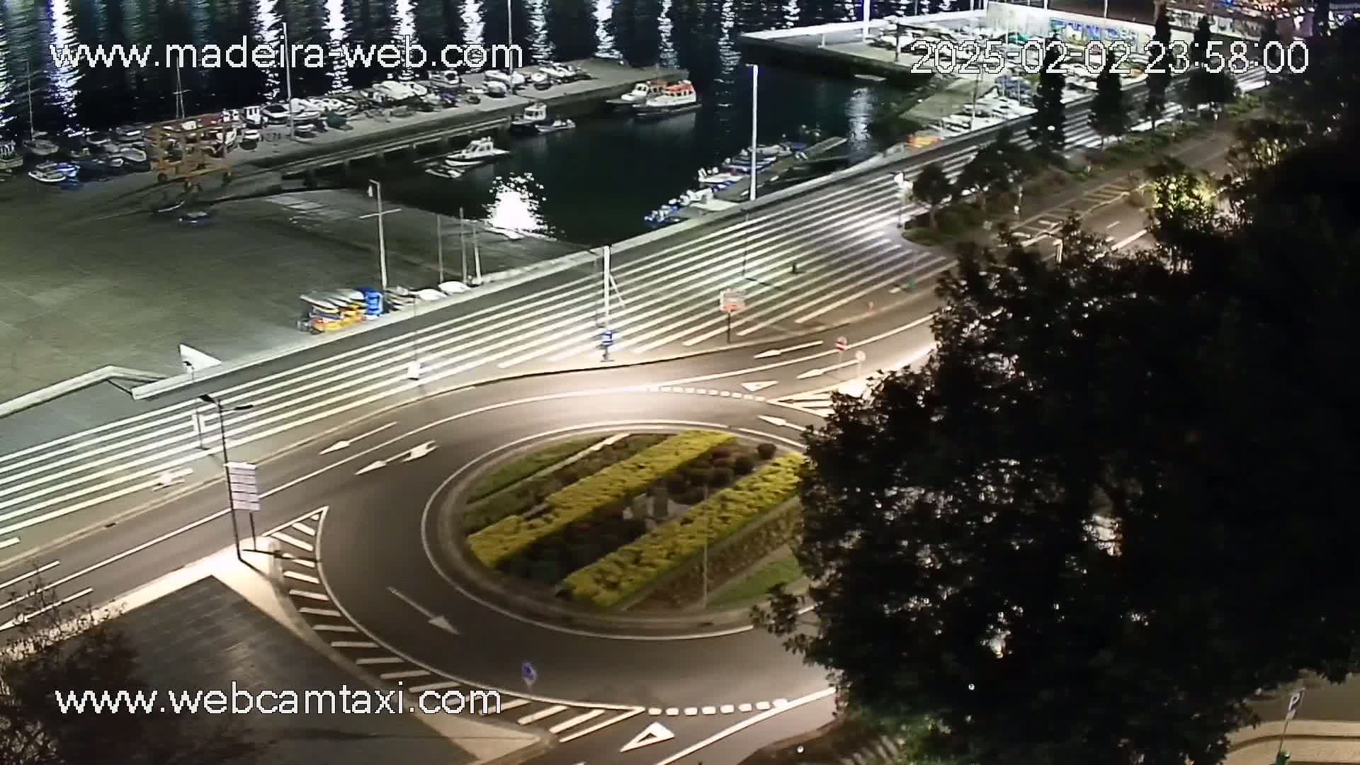 An illuminated roundabout at night next to a marina filled with boats, under a dark sky.