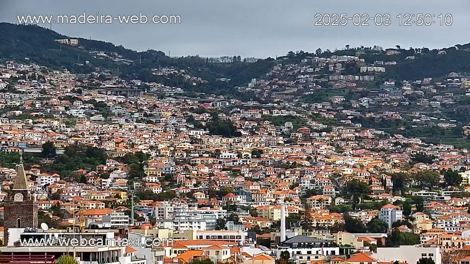 A densely populated hillside town with many closely-spaced buildings under an overcast sky.
