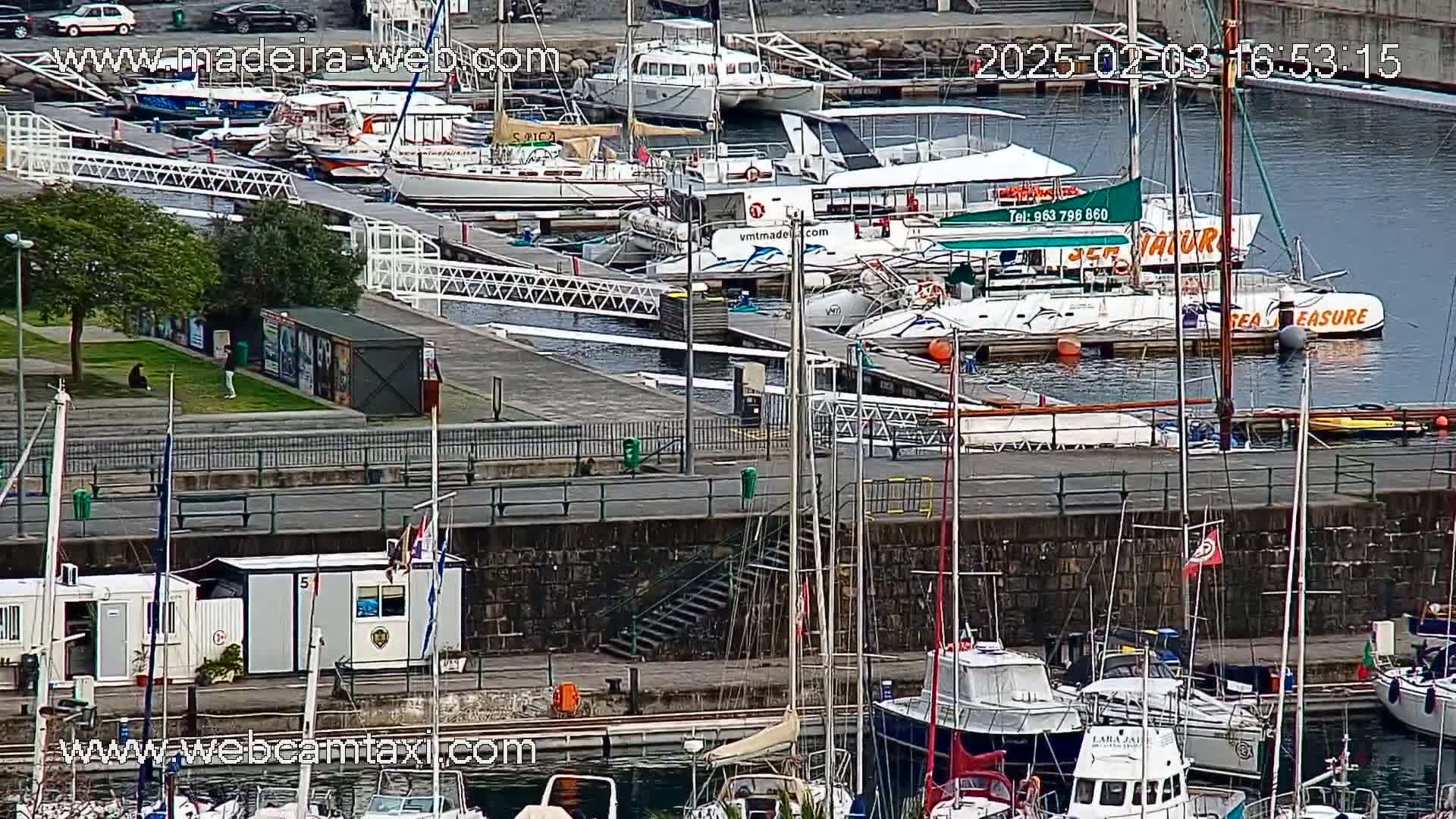 A marina filled with numerous boats of various sizes, docked along a stone wall on a partly cloudy day.