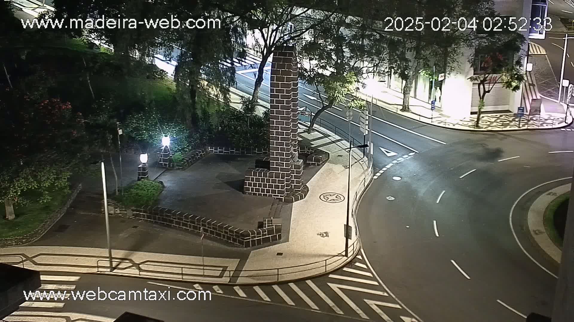 At night, a brick monument sits in a small plaza next to a curving roadway with pedestrian crosswalks.