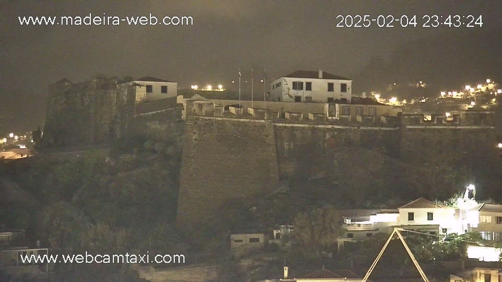 A nighttime view of a stone fortress overlooking a town, under a dark, overcast sky.