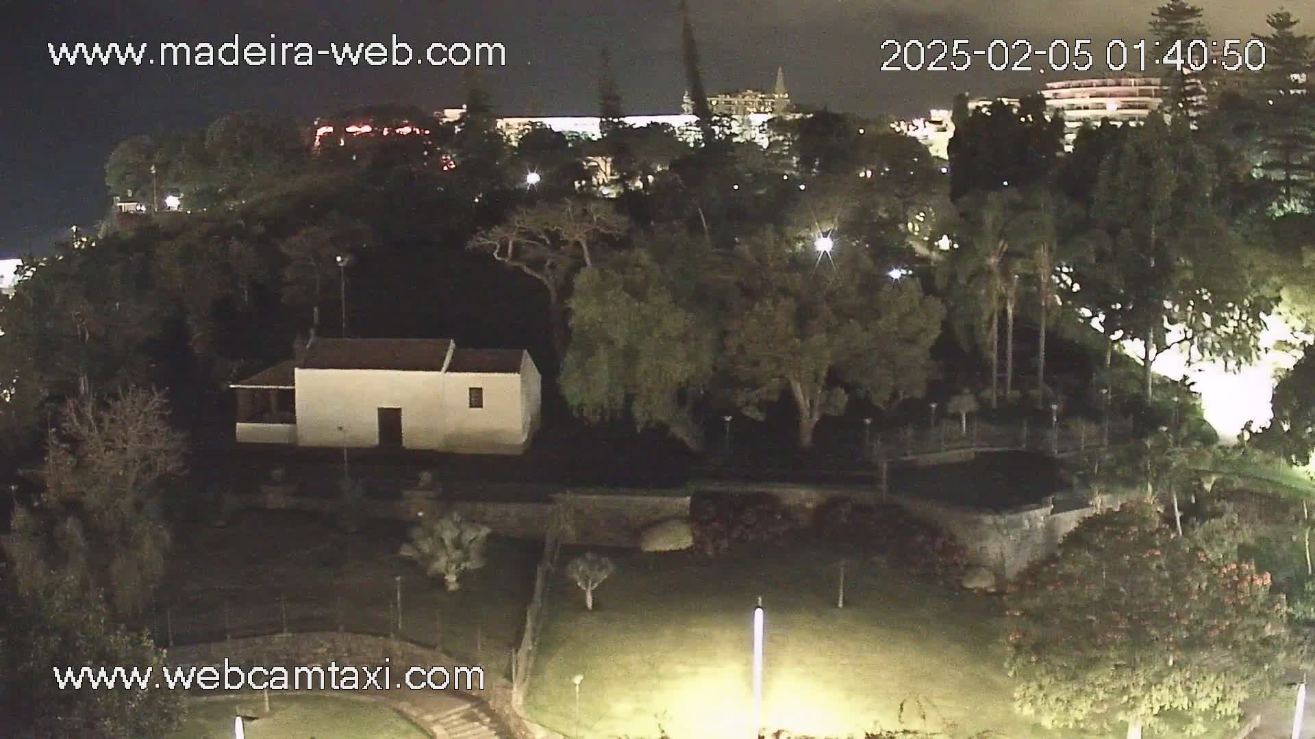 A nighttime, aerial view of a park with a small white building, trees, and low lighting.