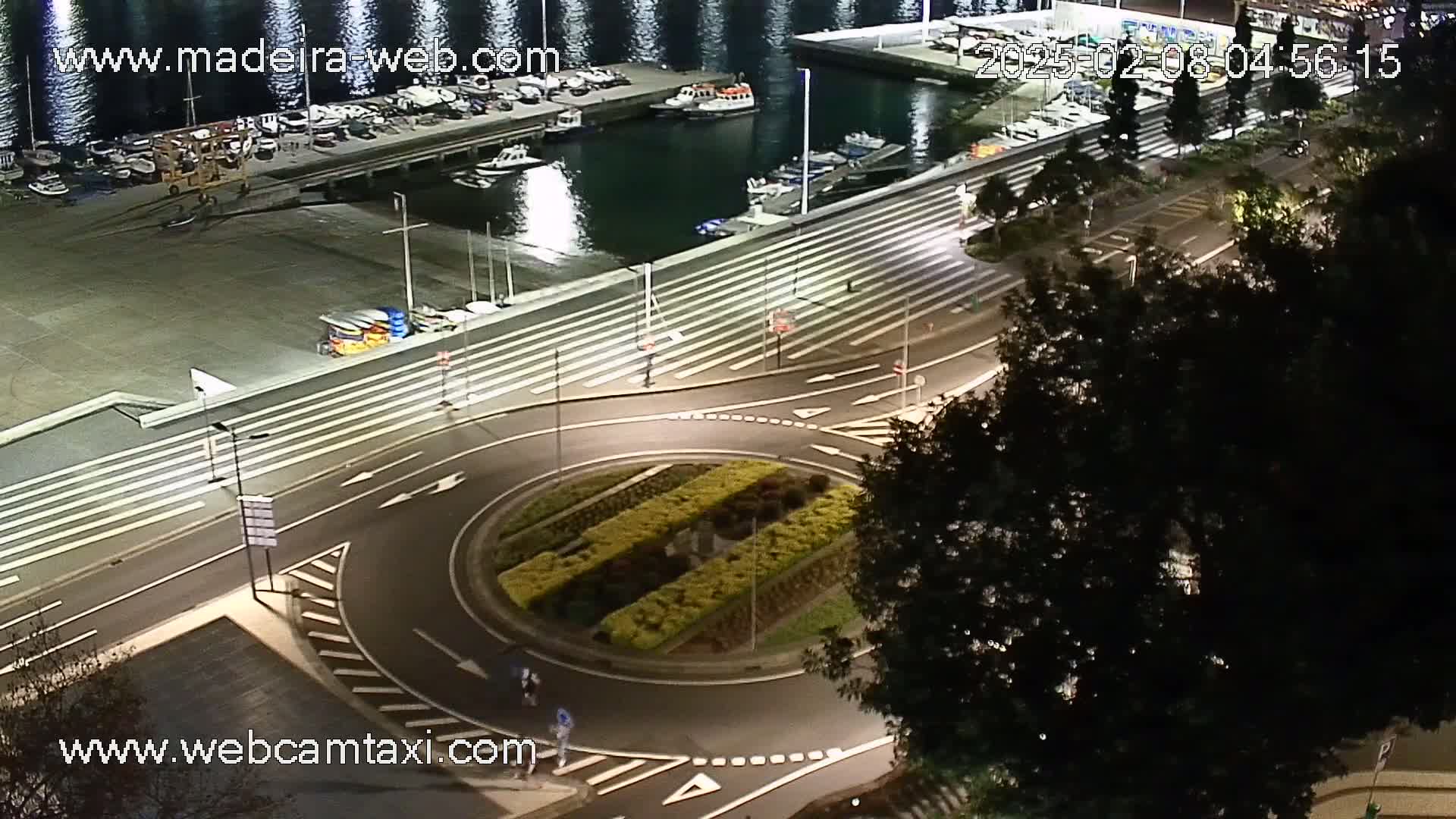 An illuminated roundabout at night next to a marina with boats docked, under a dark sky.