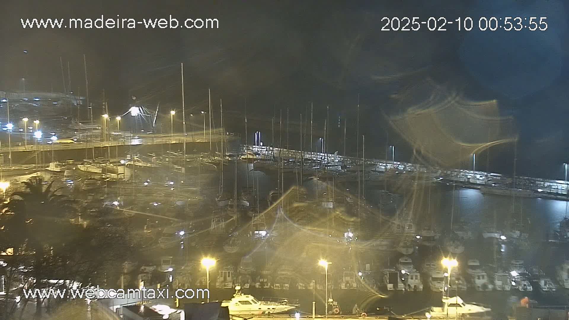 A nighttime view of a marina filled with boats in rainy, windy conditions.