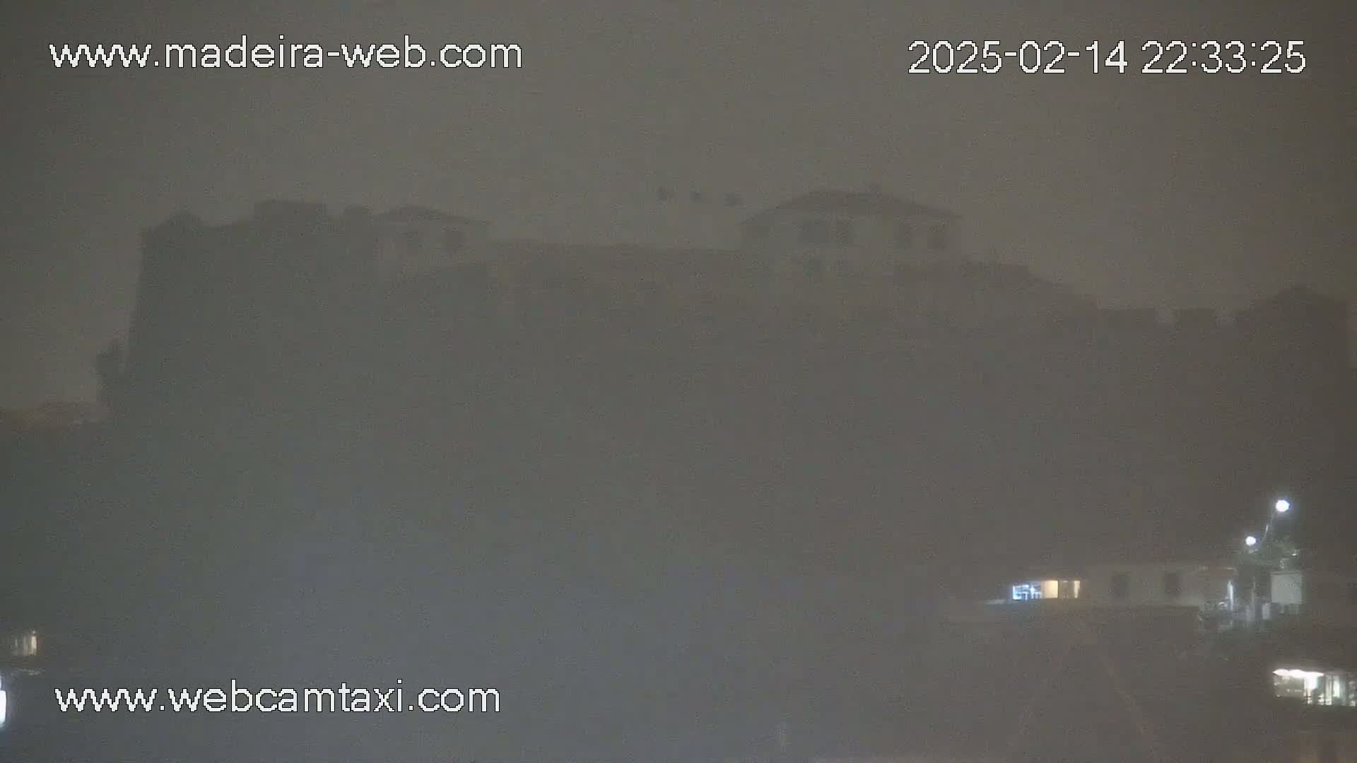 A dimly lit, foggy night scene shows buildings silhouetted against a hazy sky.