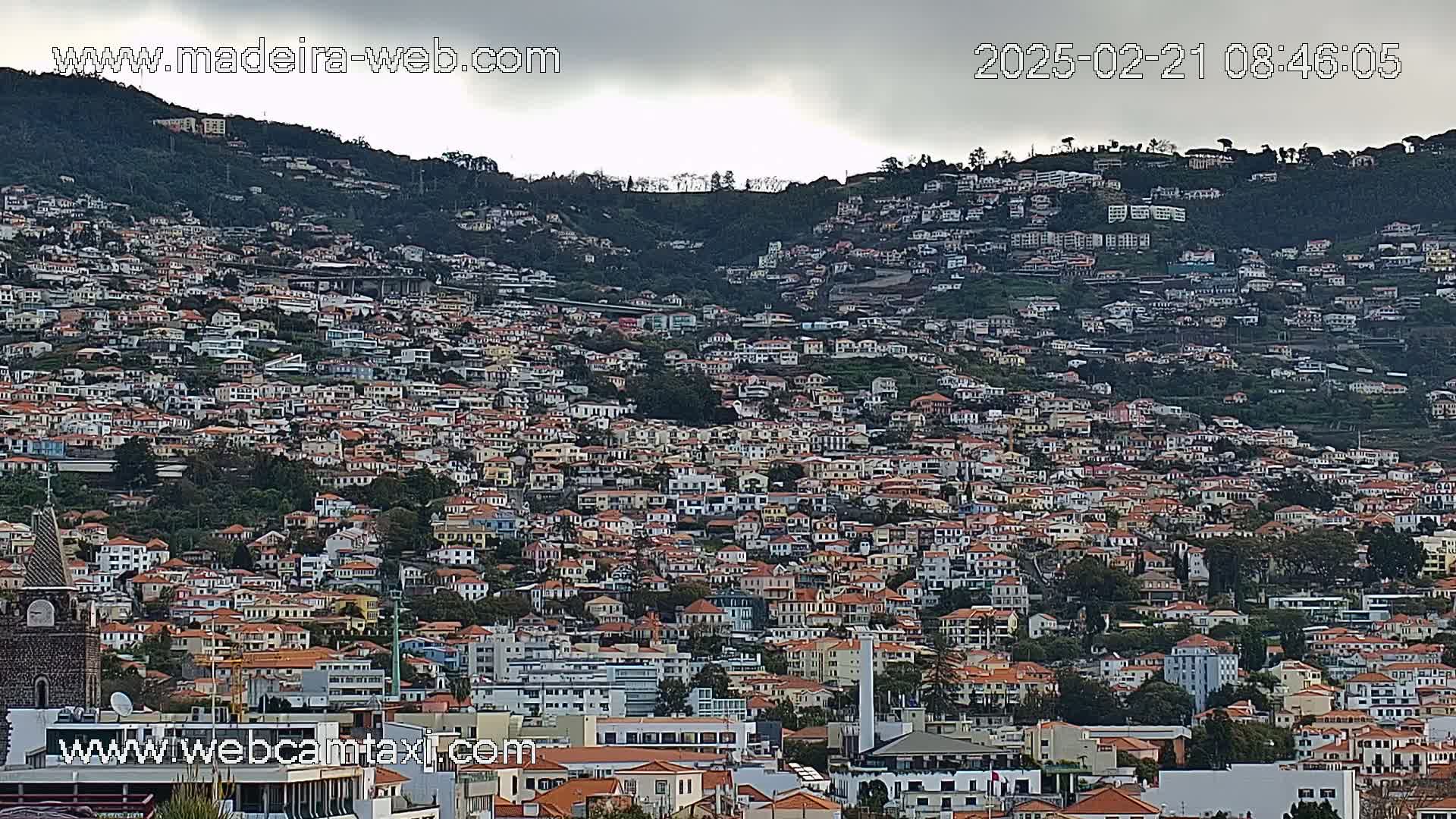 A densely populated hillside town is visible under an overcast sky.
