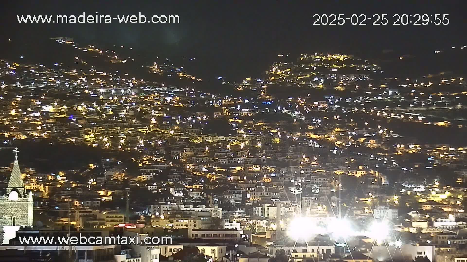 A nighttime view of a densely populated hillside town, illuminated by numerous lights.