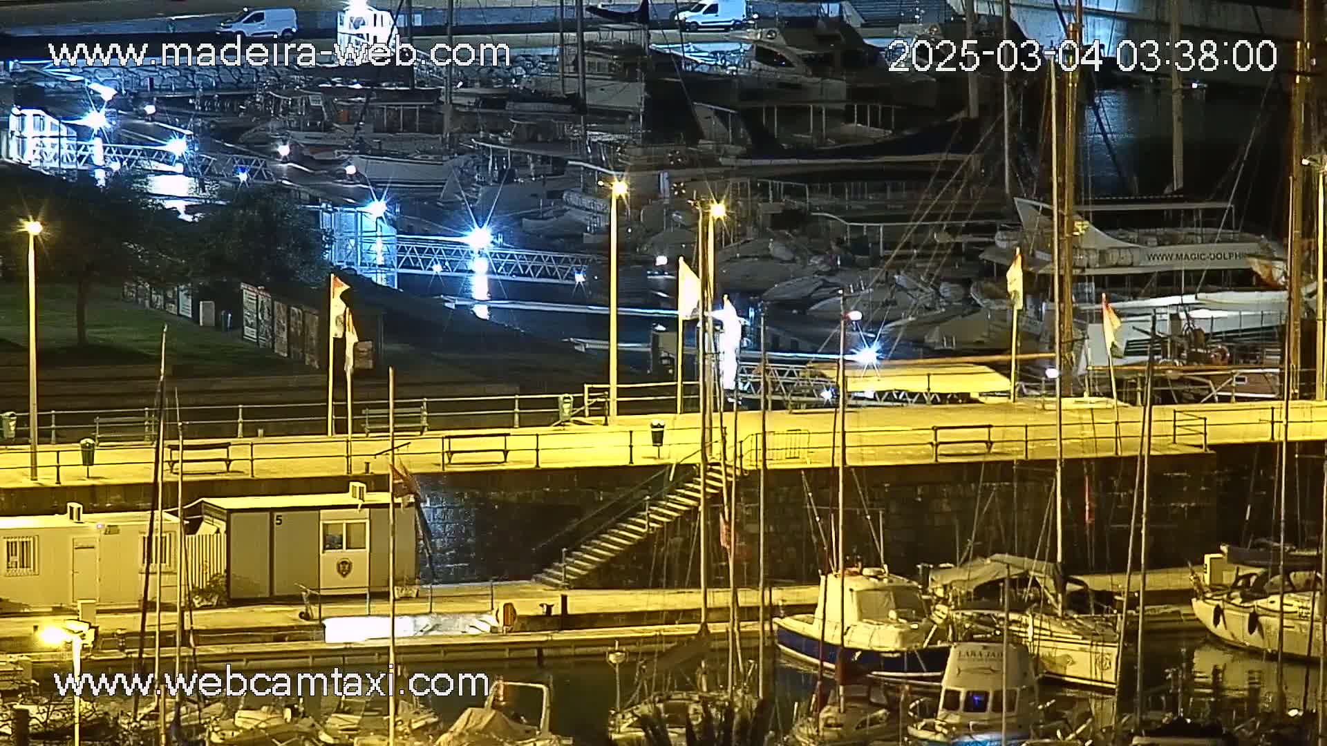 A nighttime view of a marina with many boats docked, illuminated by artificial lights.