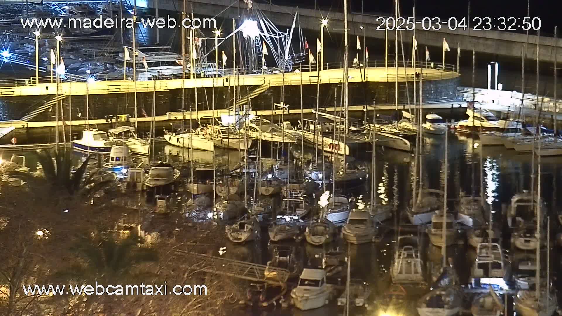 A marina at night filled with numerous sailboats and motorboats docked along a pier, under calm conditions.