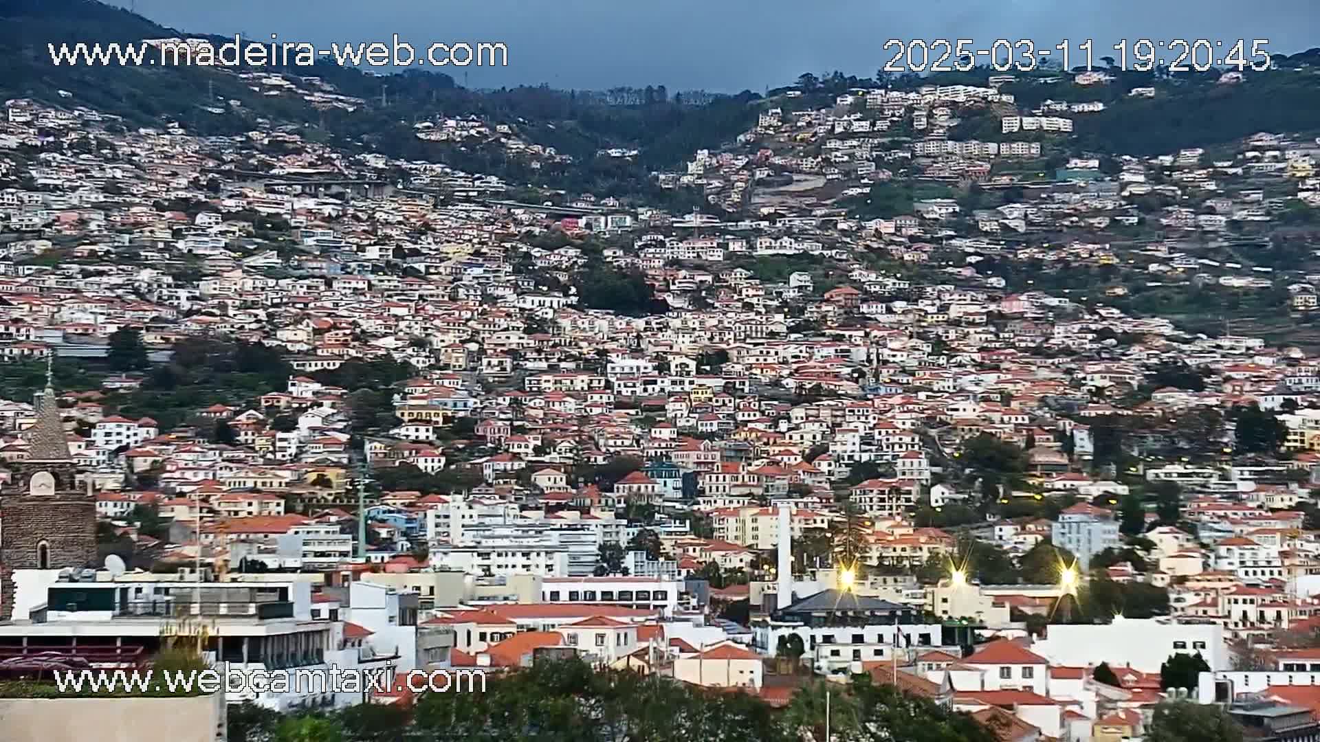A densely populated hillside town with many closely packed buildings, under a twilight sky.
