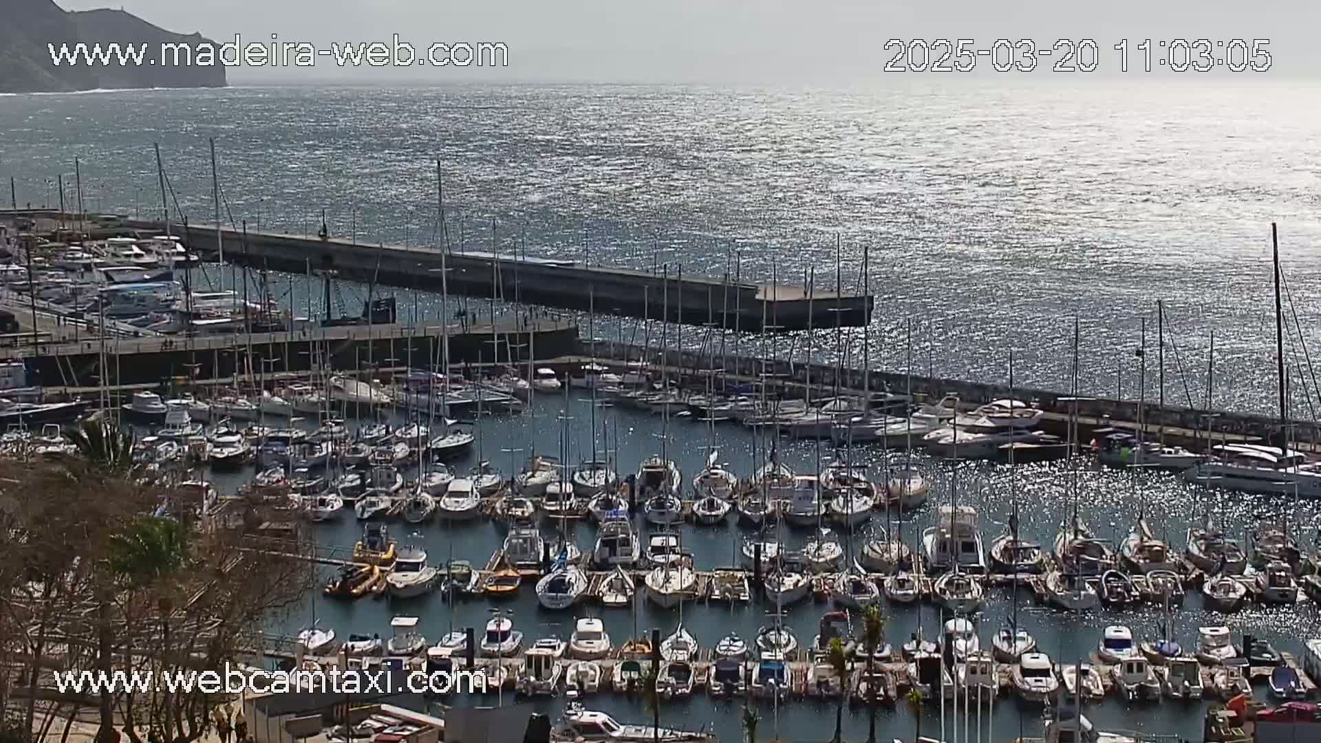 A harbor filled with numerous sailboats and motorboats on a sunny day with a slightly wavy sea.