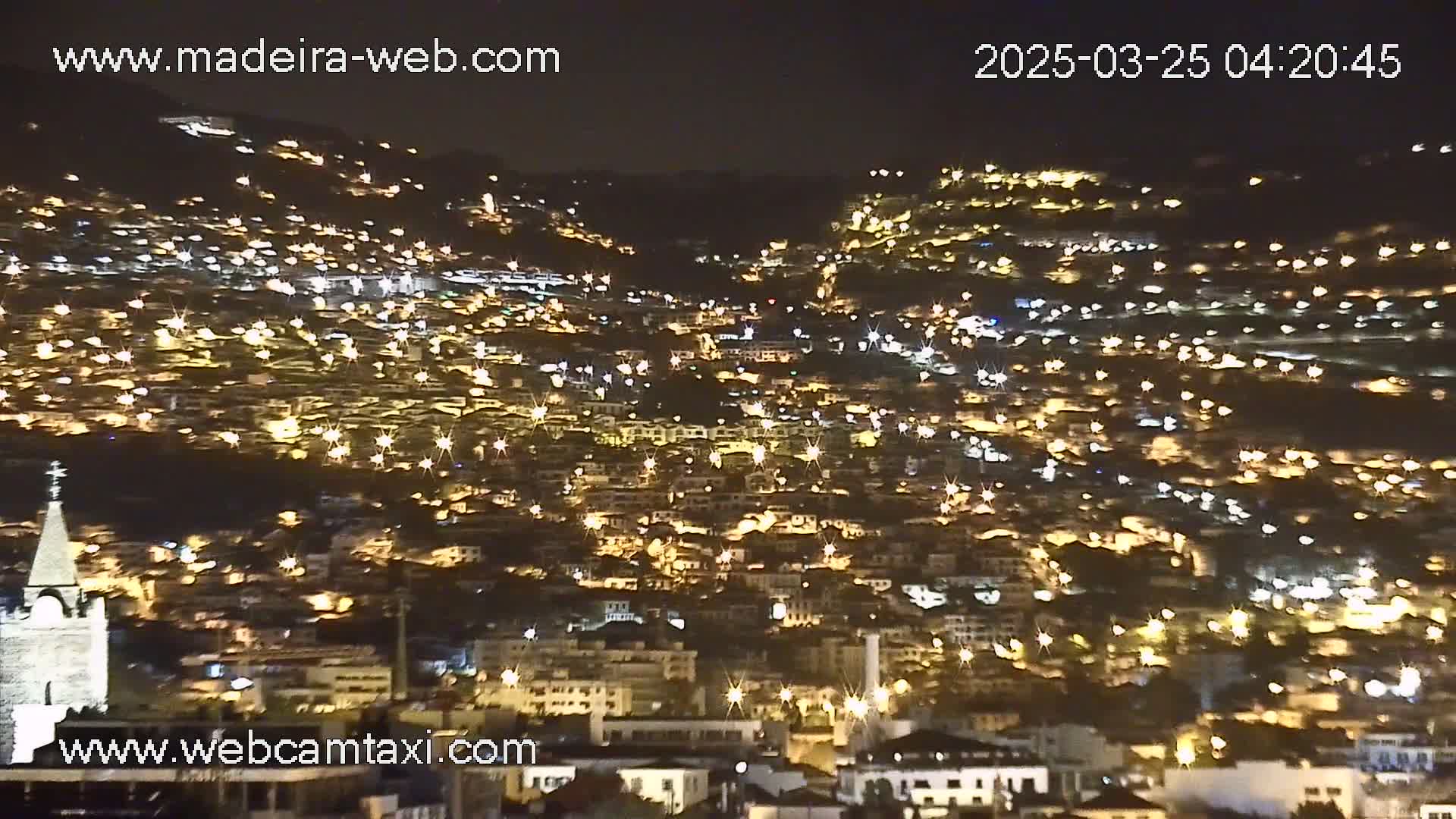 A hillside town at night is brightly illuminated by countless lights.