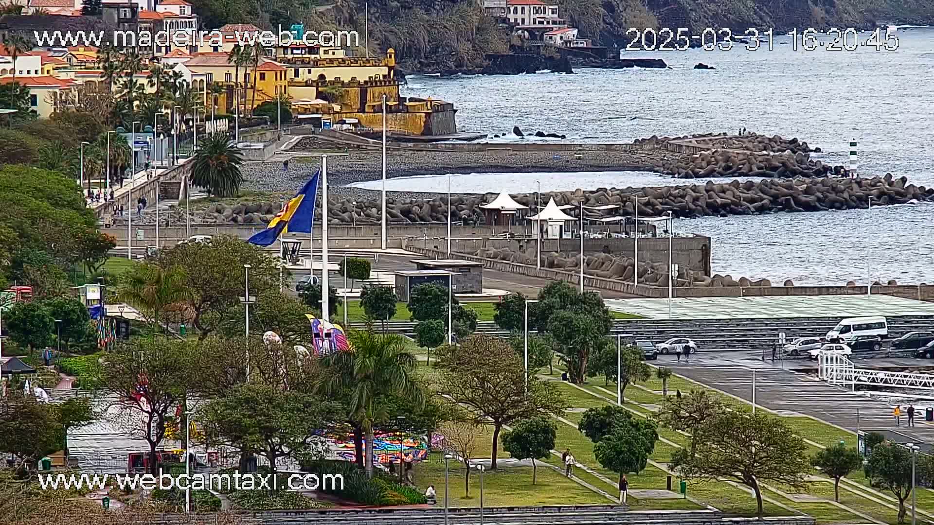 An overcast day reveals a coastal town with a park, a rocky shore, and a body of water.