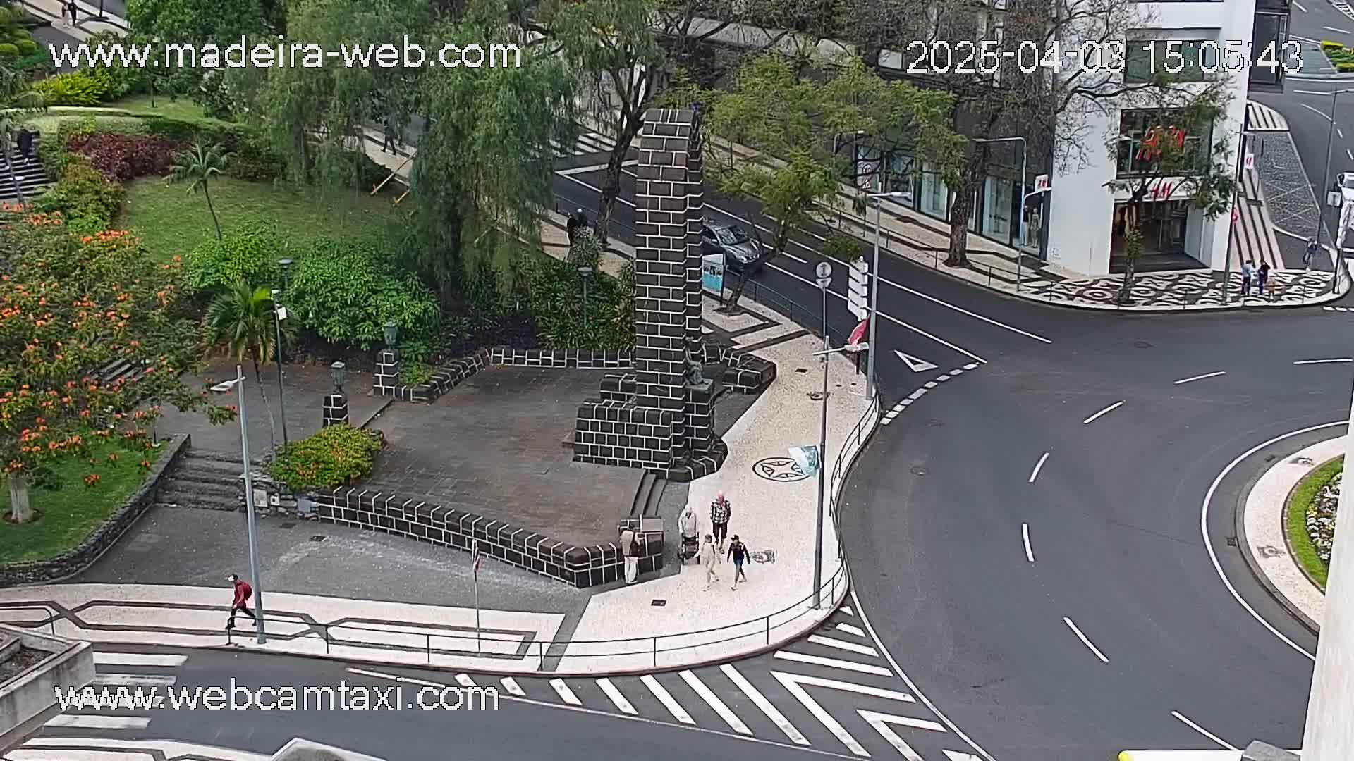 An overhead view of a city square with a brick monument, a few pedestrians, and a curving road on an overcast day.