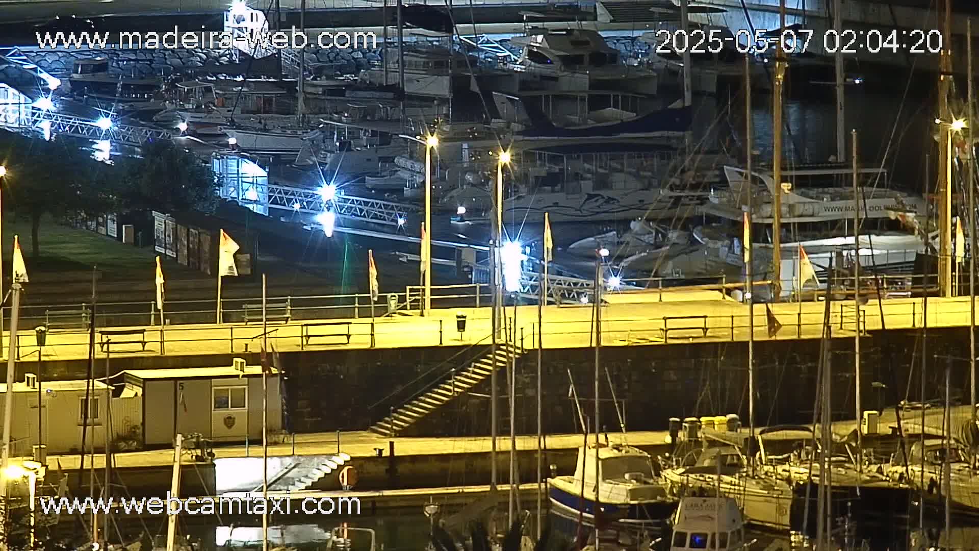 A nighttime view of a marina filled with boats, illuminated by lights, with a walkway and stairs leading to a dock.