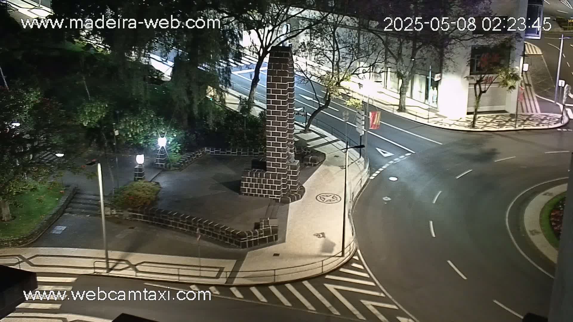A nighttime, high-angle view of a brick monument in a plaza next to a curving roadway and buildings.