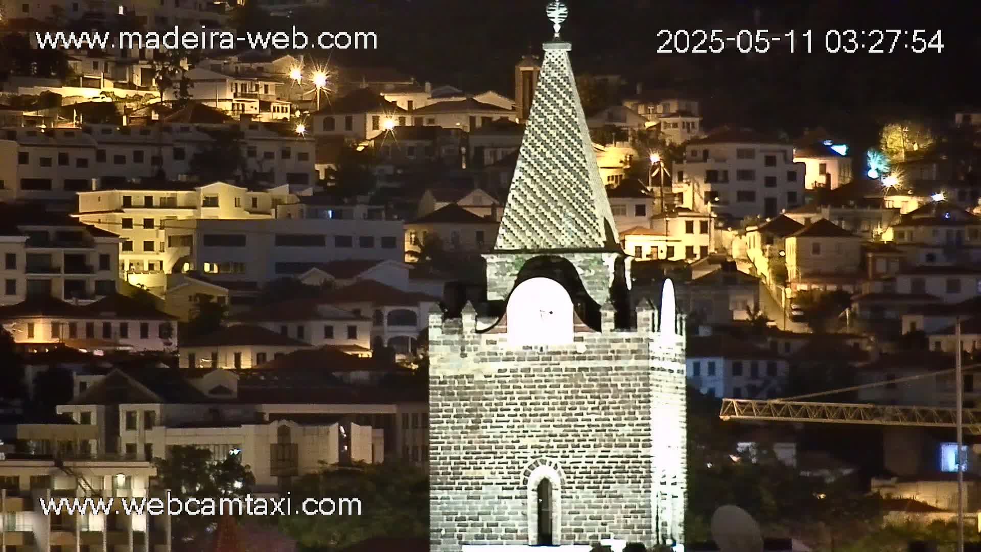 A stone tower is illuminated at night, overlooking a hillside town with many buildings lit up.