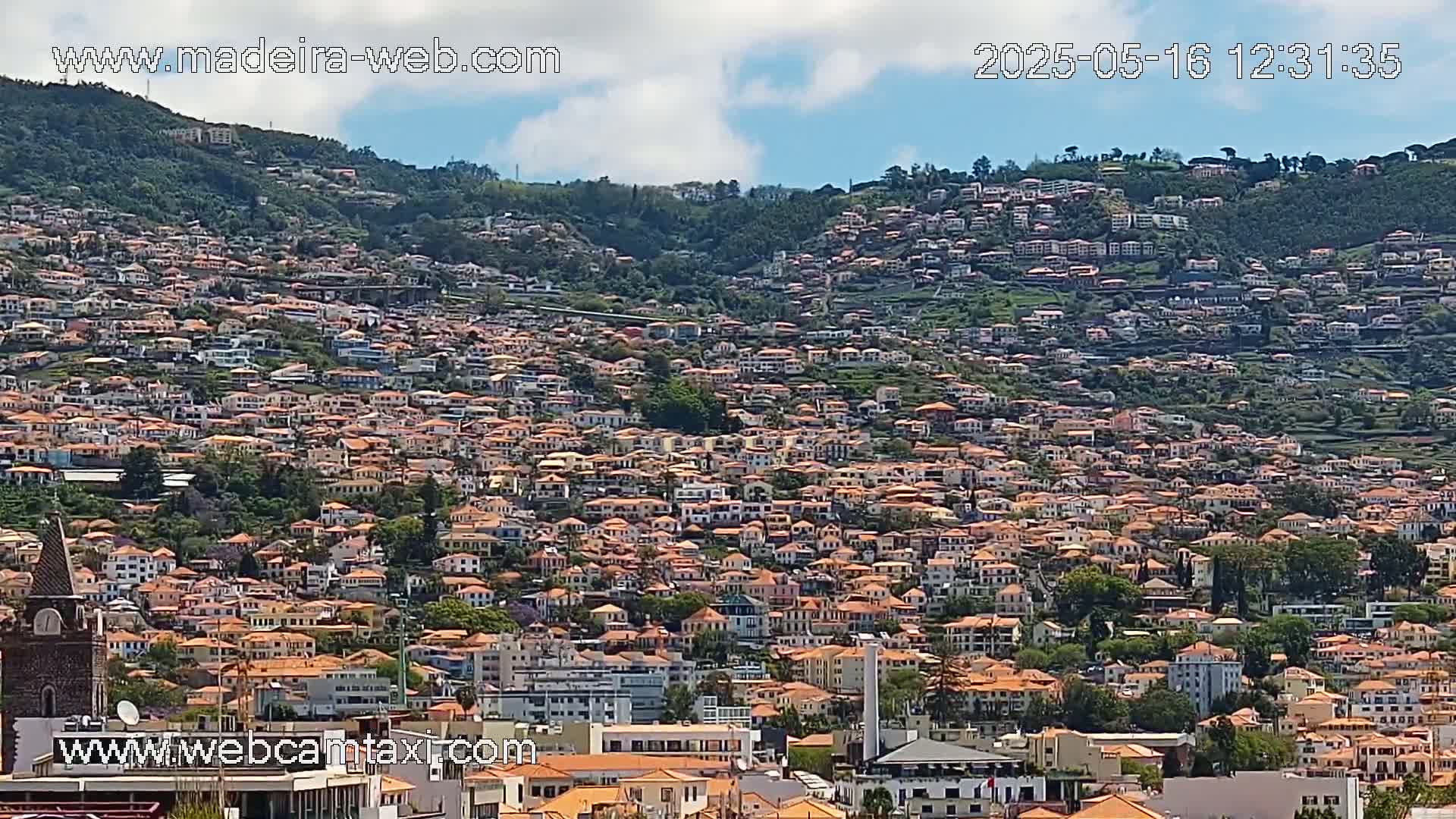 A hillside densely covered with numerous orange-roofed buildings under a partly cloudy sky.