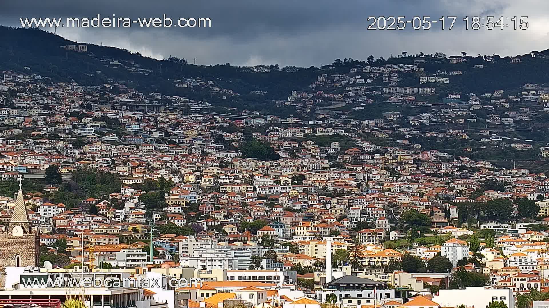 A densely populated hillside town is covered in a mix of red and white buildings under a cloudy sky.