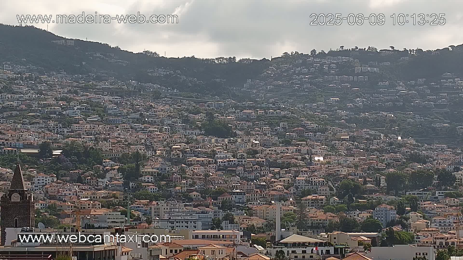 A densely populated hillside town is visible under mostly cloudy skies.