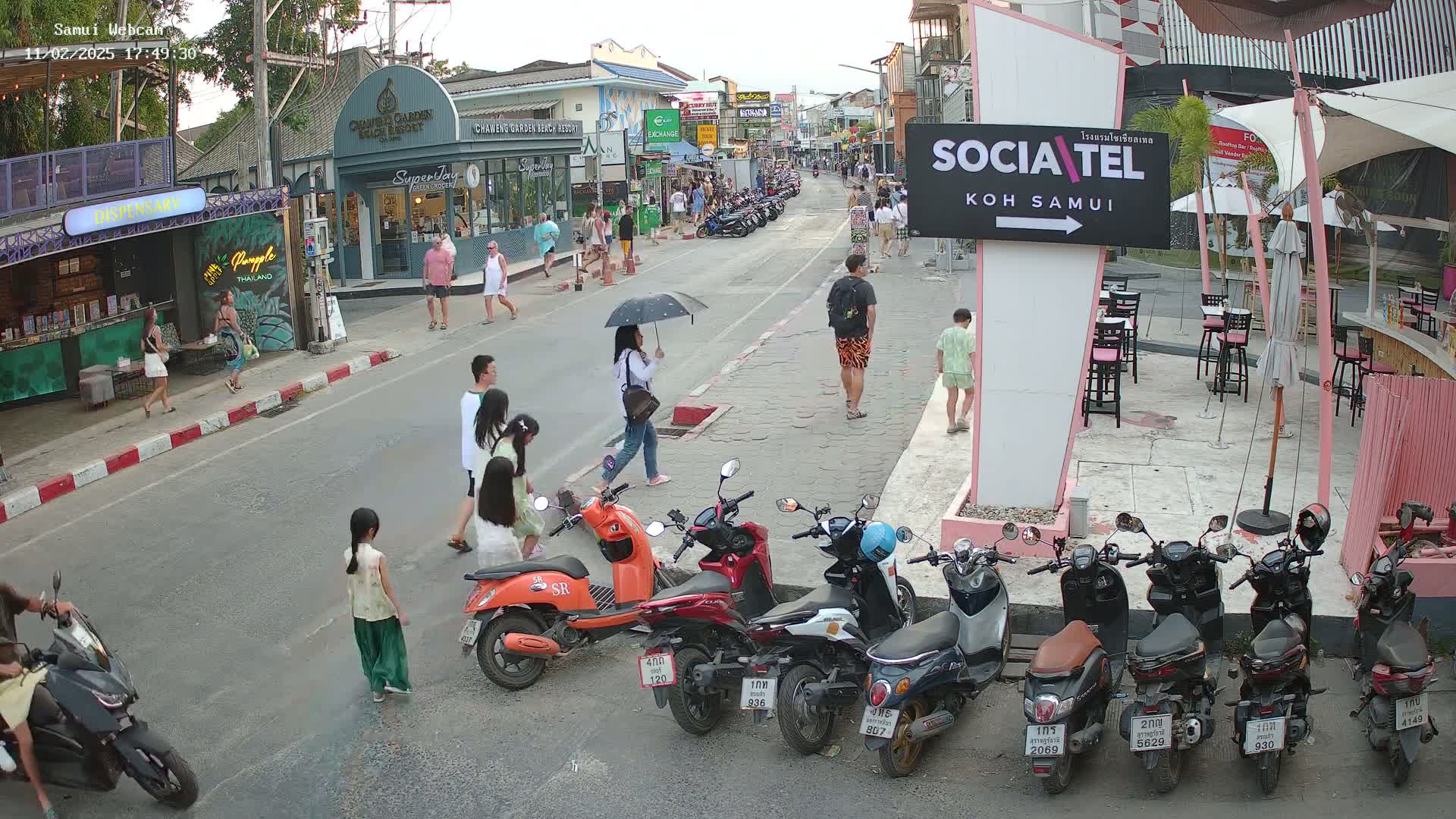 A street scene shows pedestrians and motorbikes parked along a roadway under an evening sky.