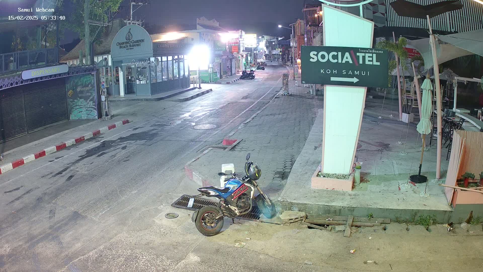 A motorcycle is parked on the side of a mostly empty street at night, with some businesses visible along the road.
