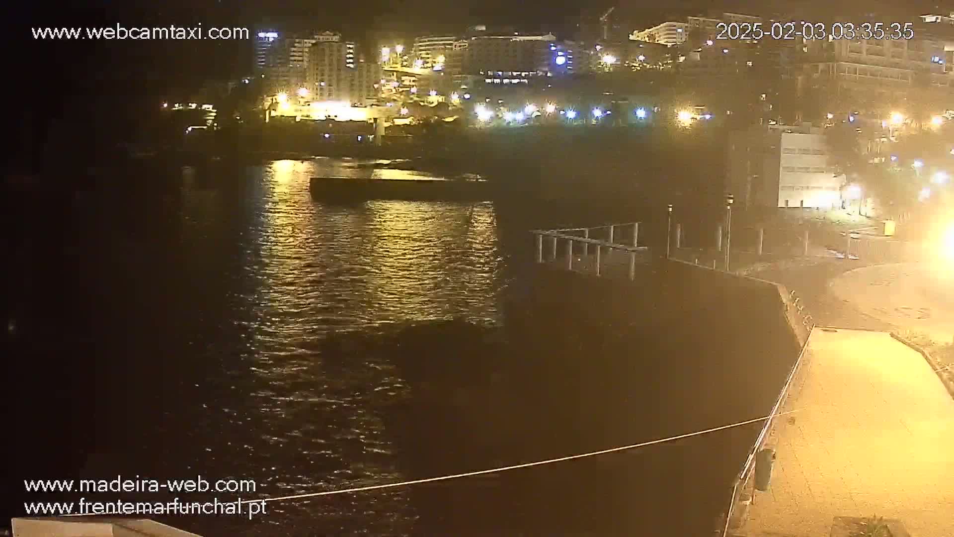 A nighttime view of a calm body of water reflecting the lights of buildings along a shoreline.