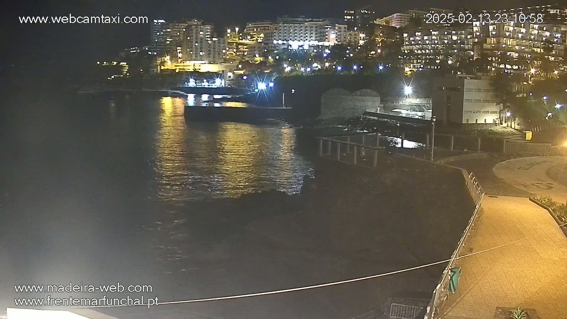 A nighttime view of a calm body of water reflecting the lights of buildings and streets along a waterfront.