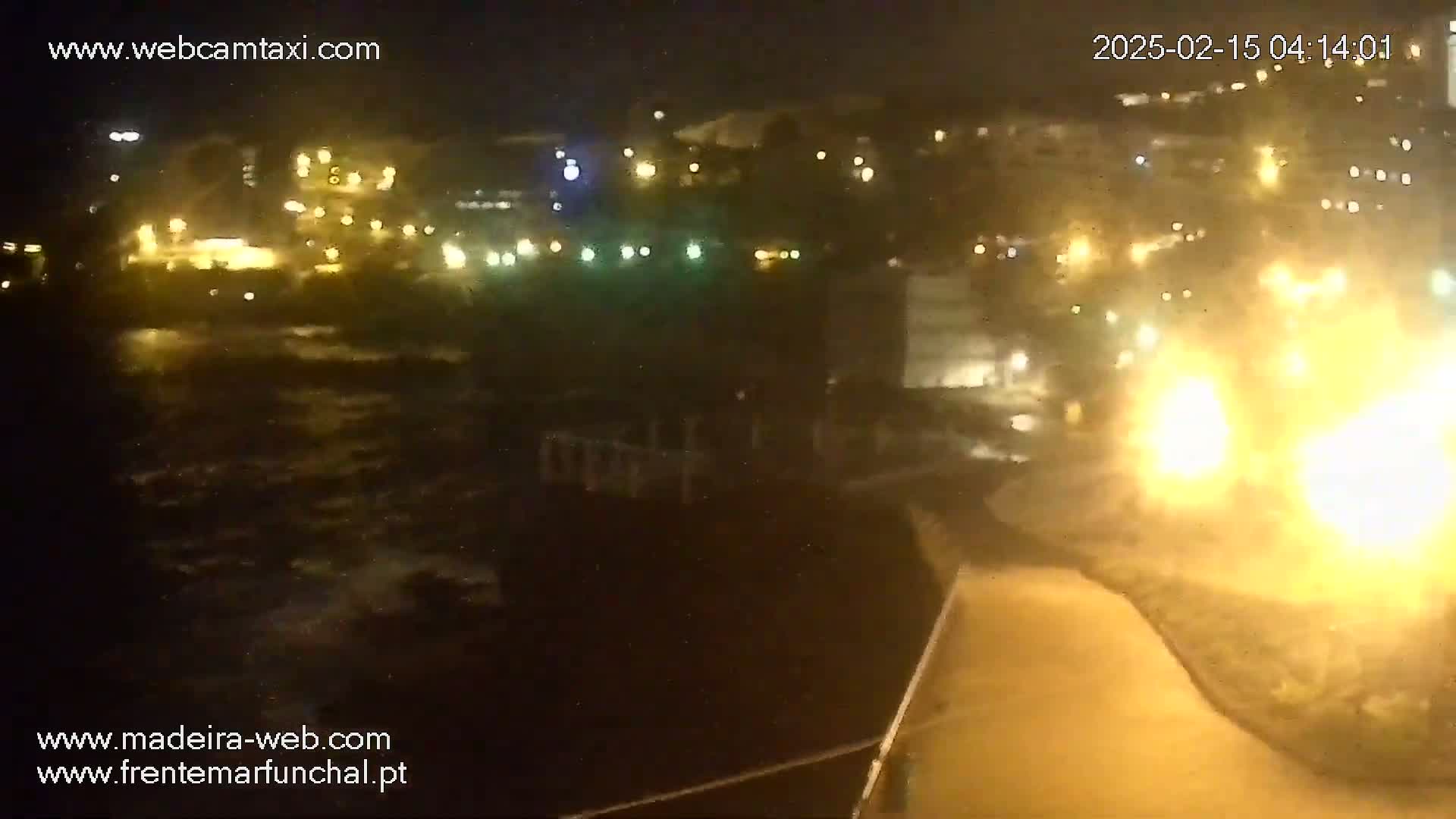 A nighttime view of a coastline with a town's lights illuminating the dark water and shoreline.