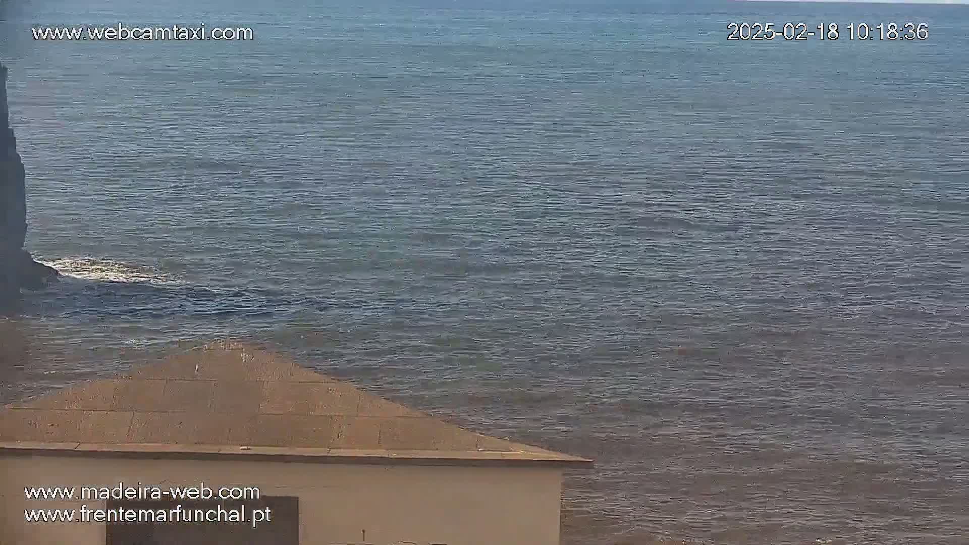 A flat, gray-blue ocean is visible from atop a low, light-brown building on a calm day.