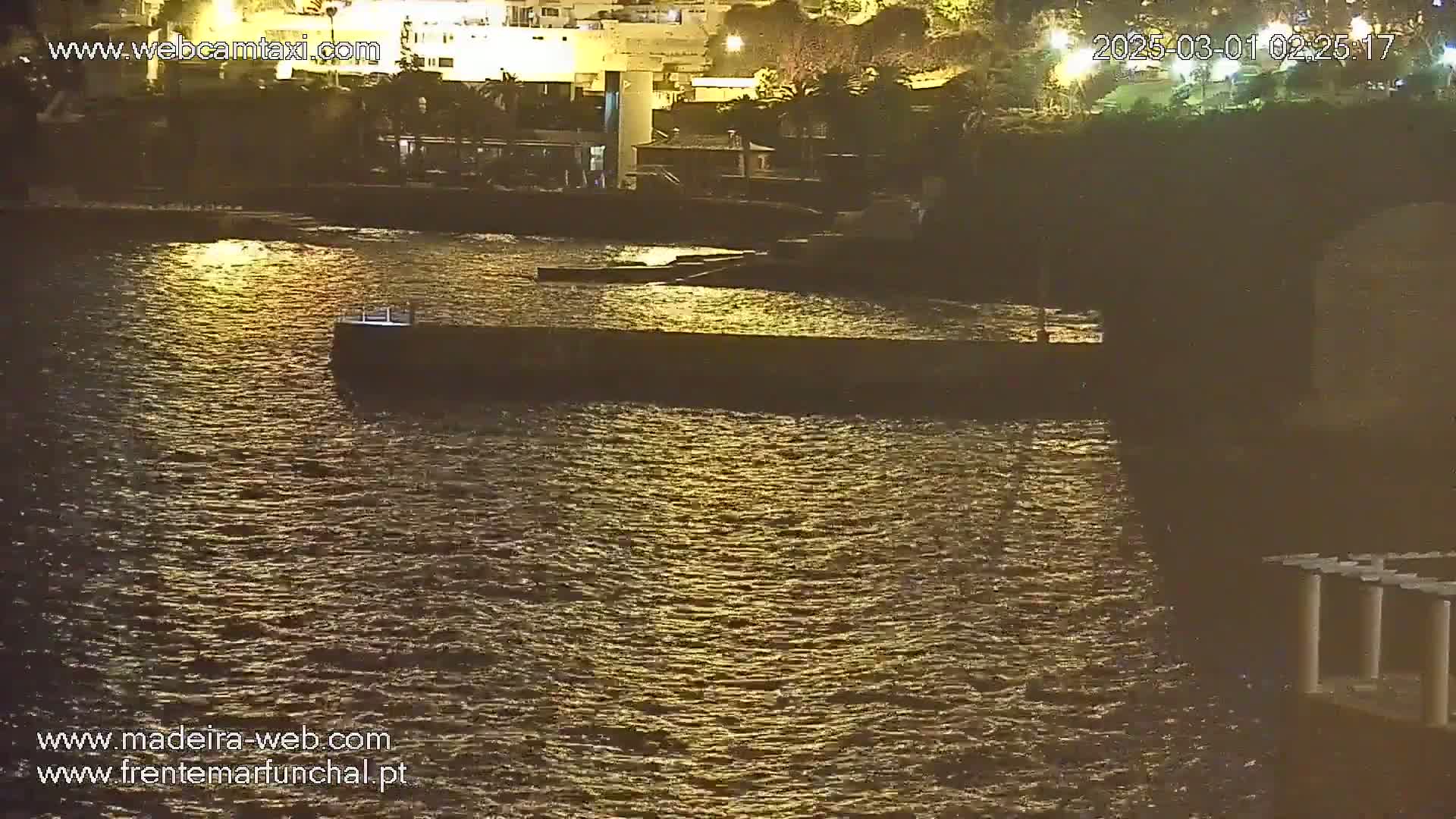 A nighttime view of calm water reflecting lights from buildings on the shore.