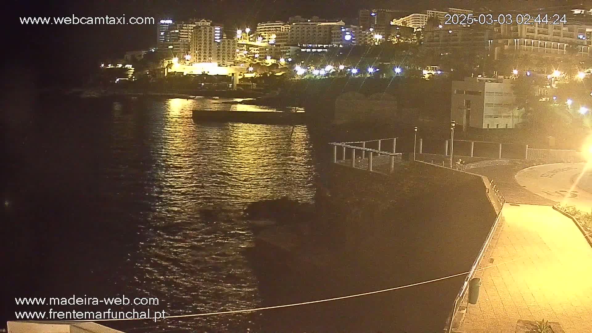 A nighttime view of a calm body of water reflecting the lights of buildings on a nearby shore.