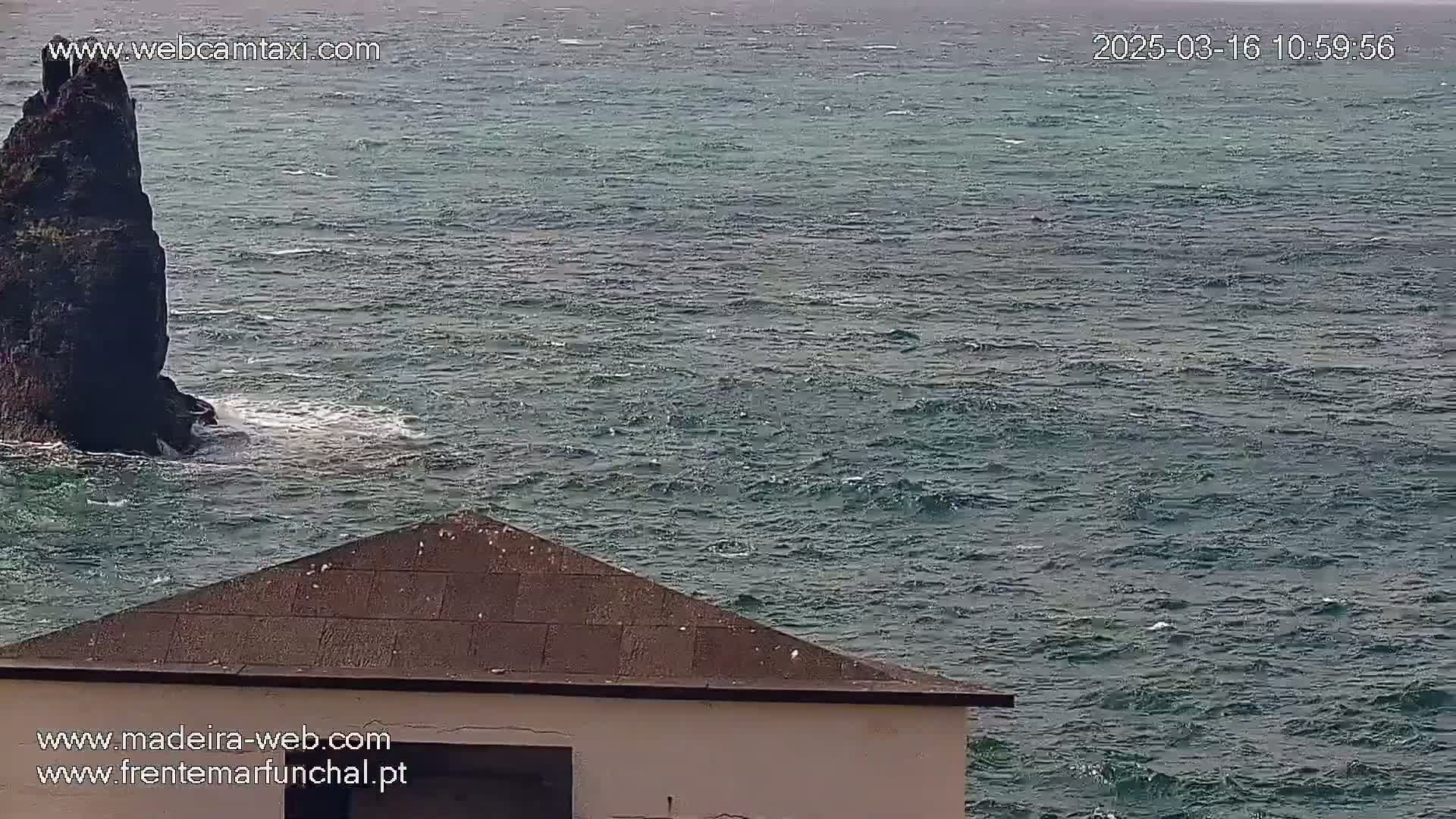 A dark, rocky outcrop juts out of a choppy, dark-green sea, partially visible behind a triangular-roofed structure.