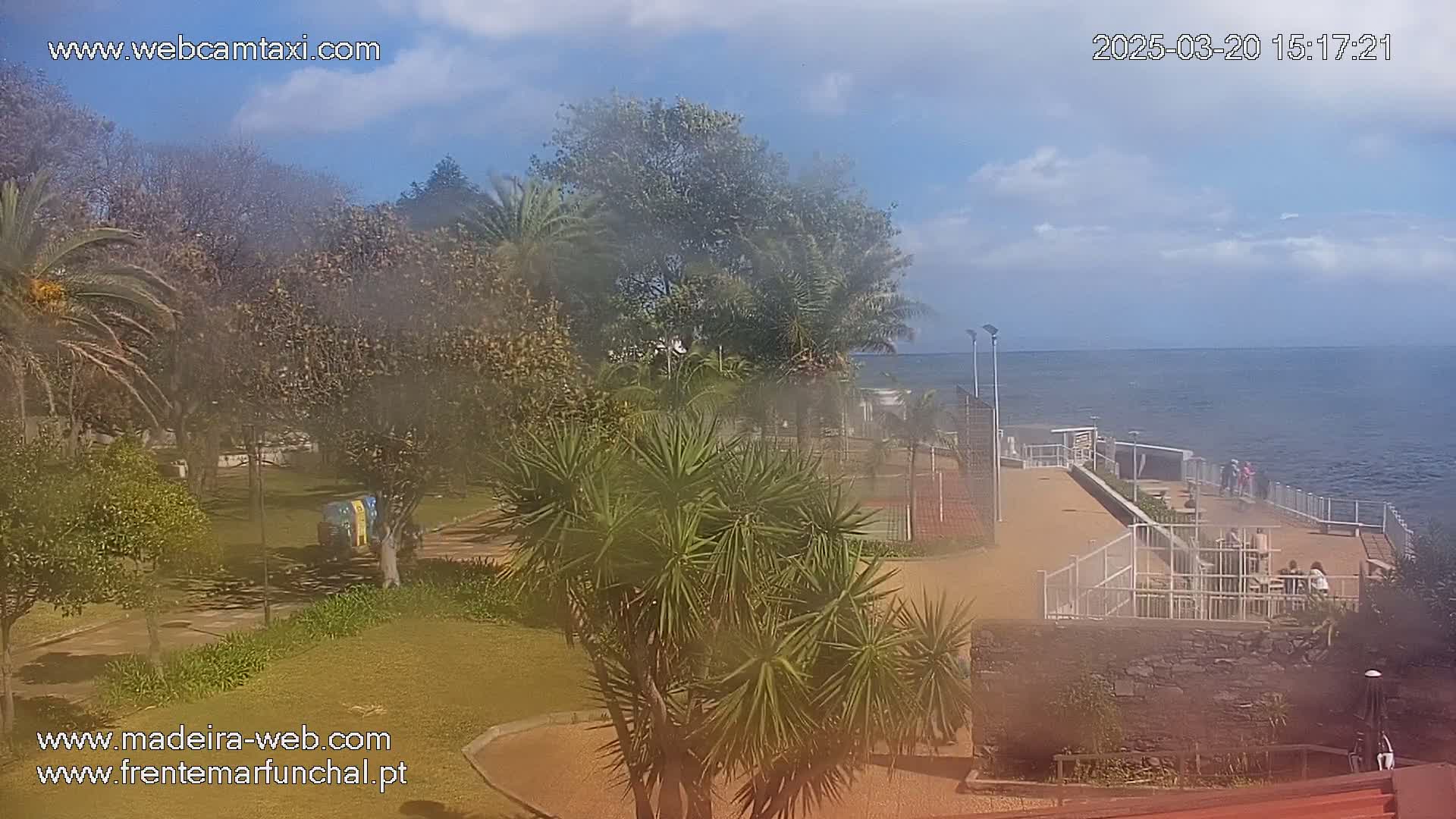 A hazy, sunny day overlooking a park and ocean, with a walkway along the coast featuring a few people.