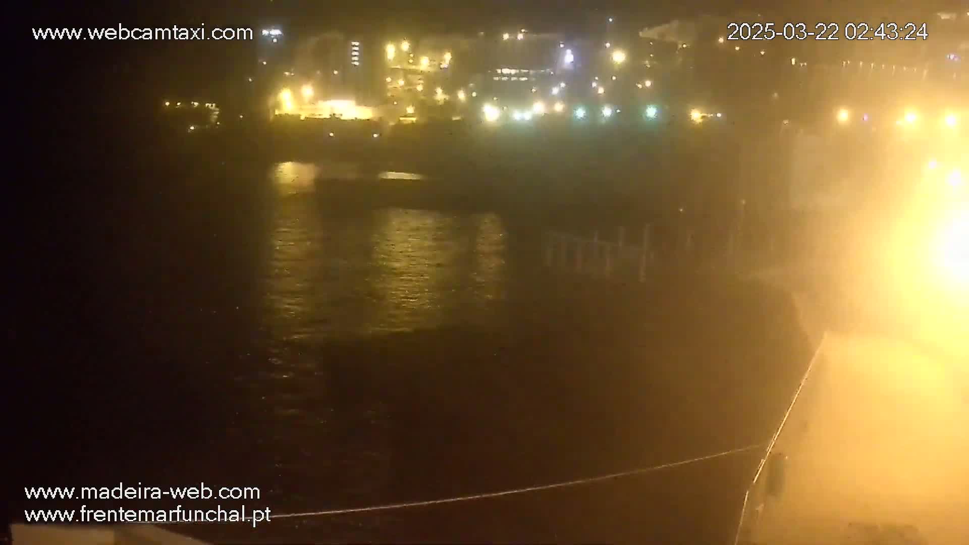 A nighttime view of a harbor with illuminated buildings across the water, partially obscured by fog or mist.