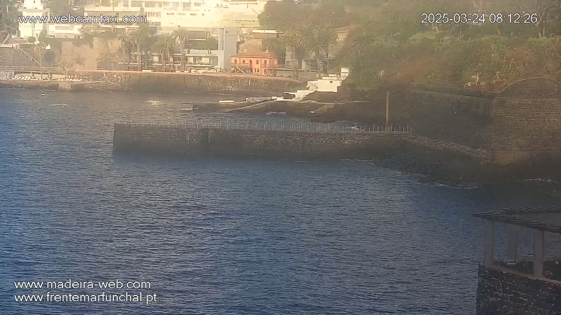 A hazy view of a calm body of water with a stone wall and buildings along the shoreline.